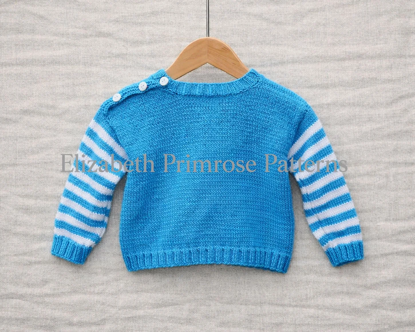 Back view of blue children jumper with striped sleeves displayed on a wooden hanger against a soft grey background.