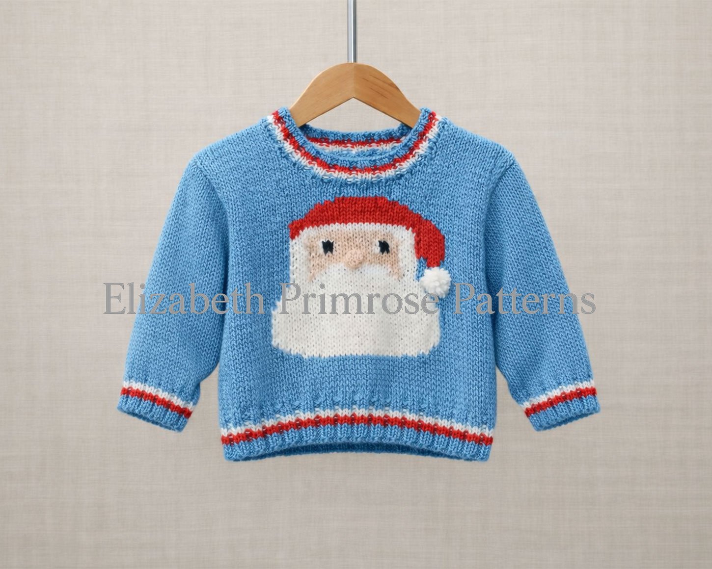 Front of a blue children’s Santa jumper on a wooden hanger, showing the bold Santa motif against a soft beige background.