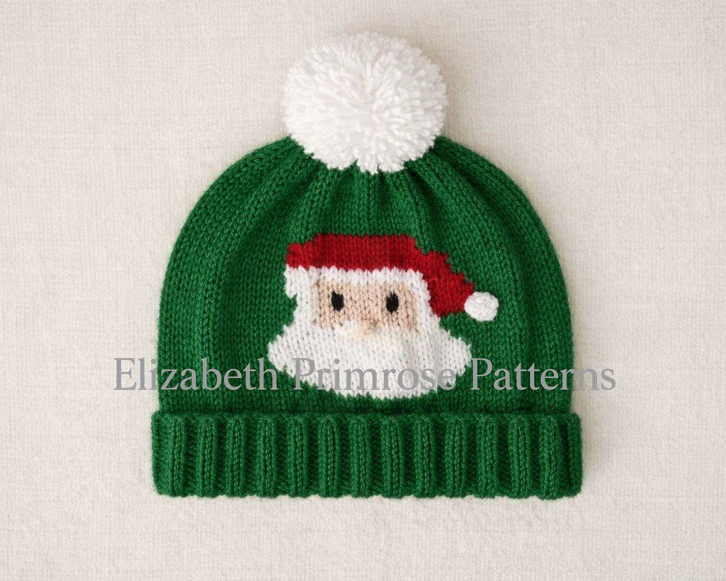 Green children’s Santa hat with folded brim and white pompom, displayed on a soft linen background.