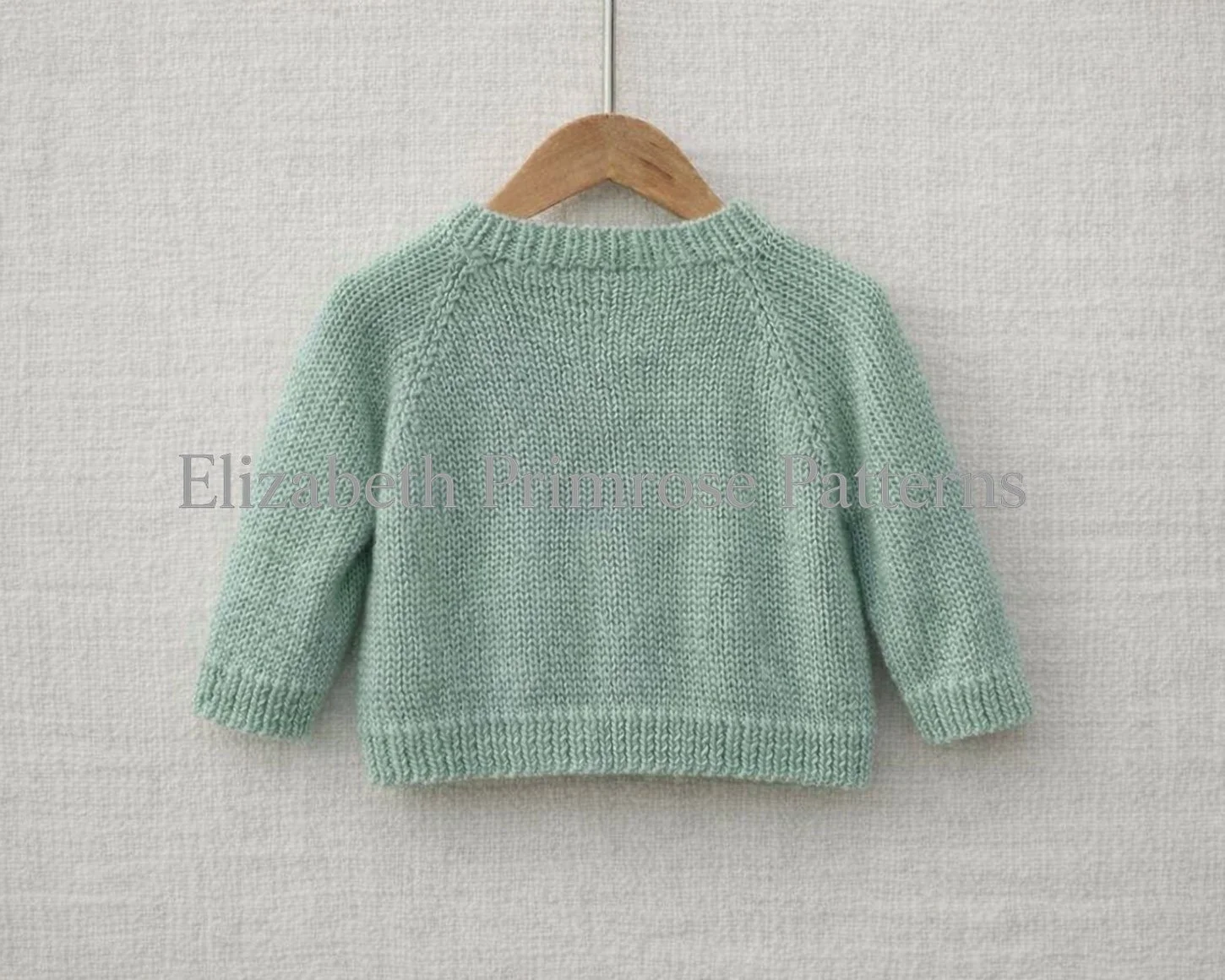 Green hand‑knitted jumper shown from the back on a wooden hanger, with ribbed cuffs, hem, and neckline against a soft neutral background.