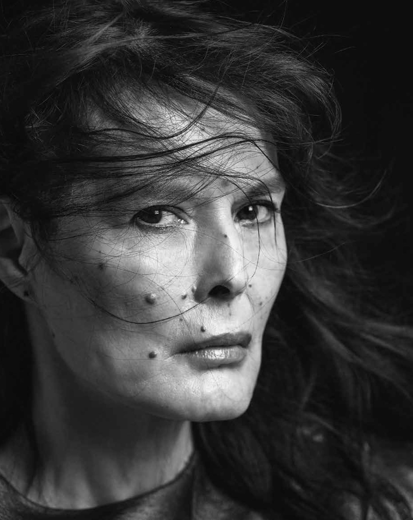 Portrait en noir et blanc d'une femme avec des cheveux en mouvement et plusieurs piercings sur le visage.