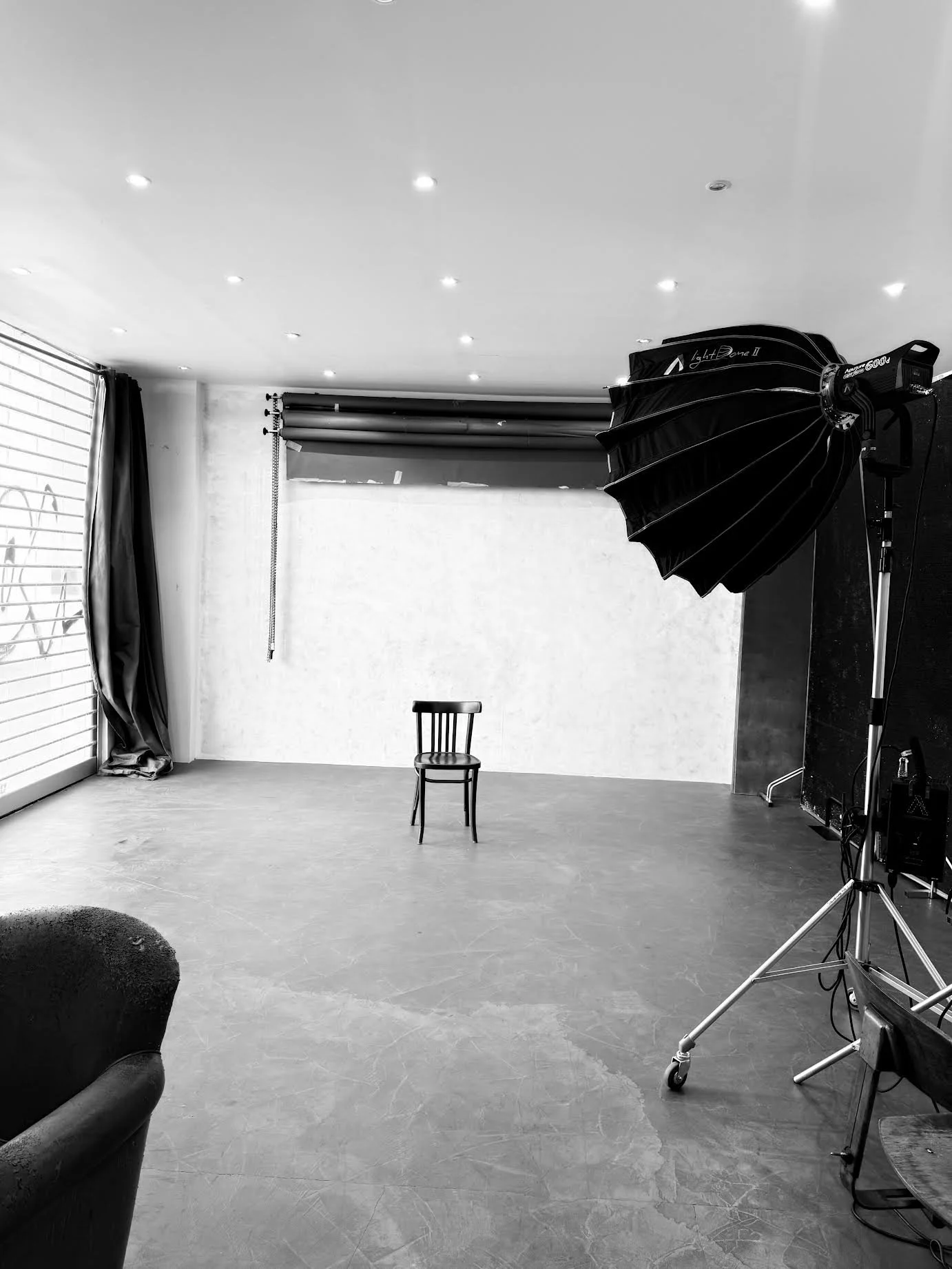 Une pièce vide d'un studio photo avec un fond blanc, un éclair de photographie professionnel, une chaise en bois au centre, et un grand lampadaire