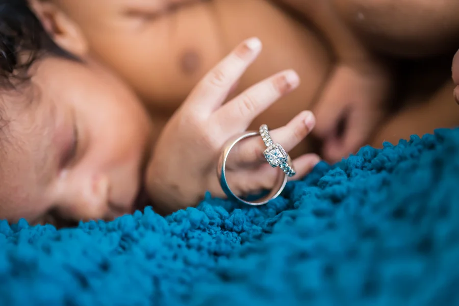 Baby sleeping on blue blanket holding parents' wedding rings