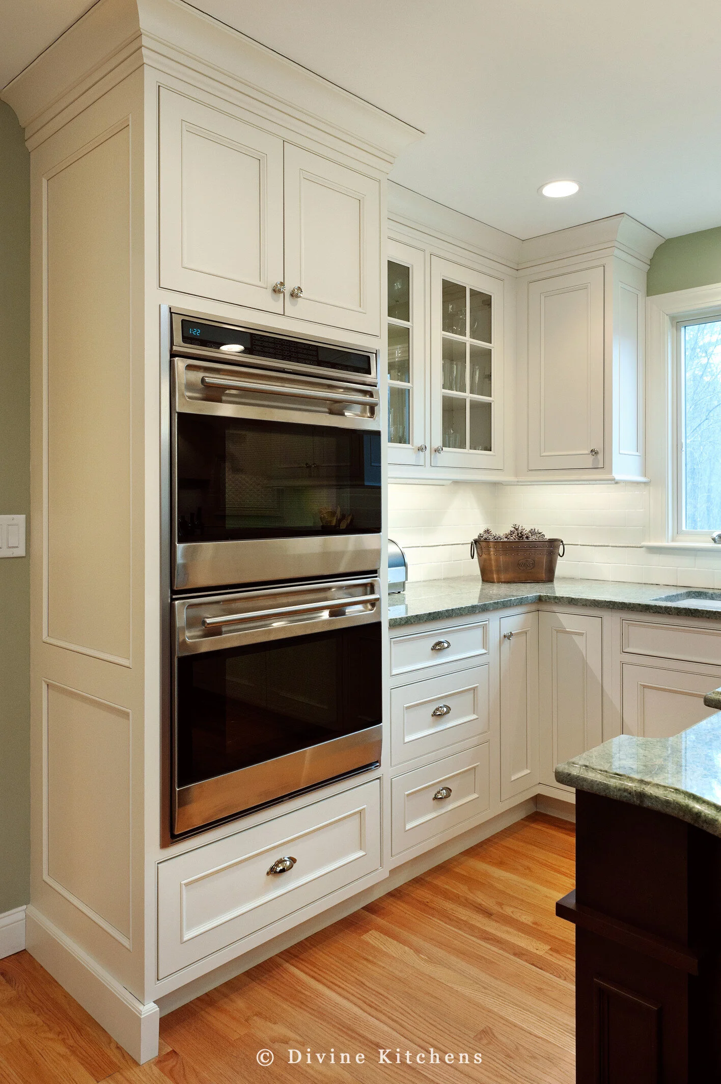 Traditional Kitchen with white shaker cabinetry and double decker appliances. Marble countertops float above a kitchen island and medium hardwood floors. A laundry room is adjacent to the kitchen.