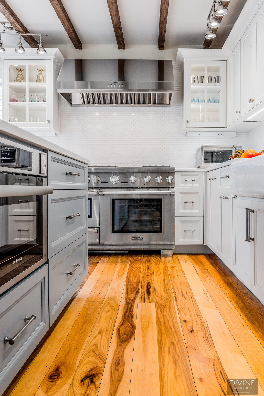 white, shaker style cabinets with brushed nickel accessories, white mosaic subway tile backsplash, cambria countertops with light marbling in grey tone. Thermador gas range, hood, and oven