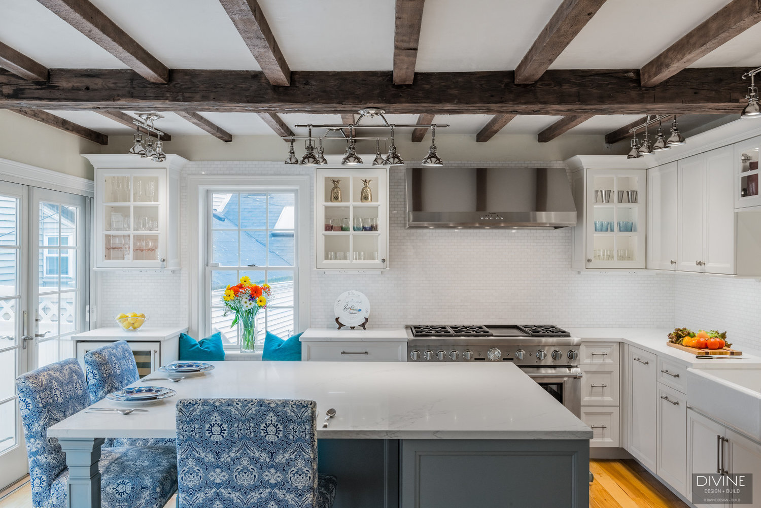 white, shaker style cabinets with brushed nickel accessories, white mosaic subway tile backsplash, cambria countertops with light marbling in grey tone and thermador appliances. Exposed beams