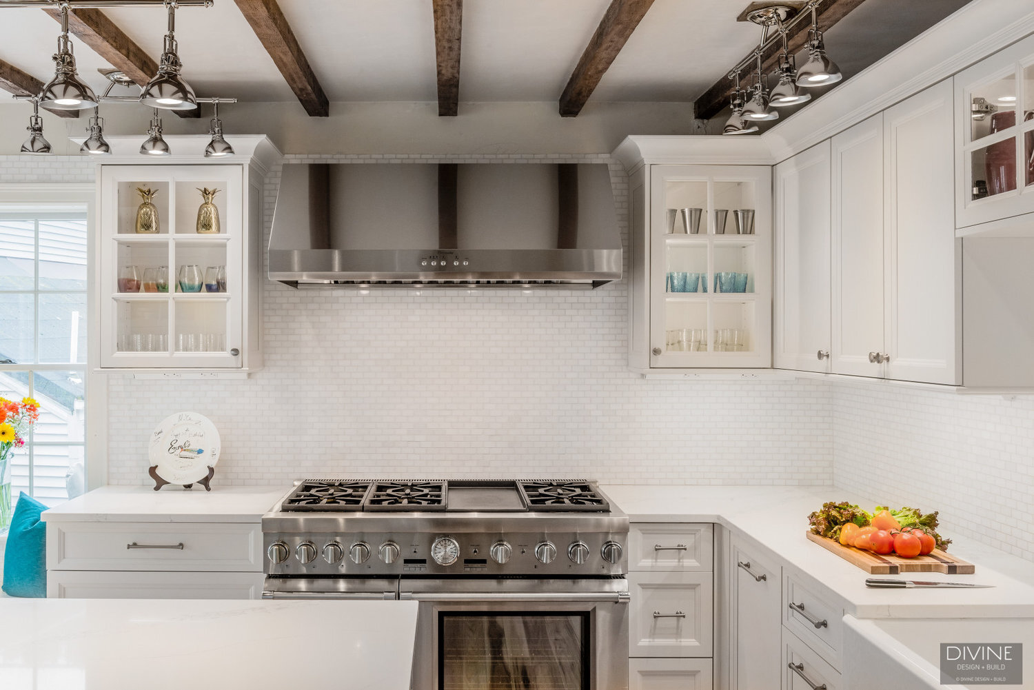 white, shaker style cabinets with brushed nickel accessories, white mosaic subway tile backsplash, cambria countertops with light marbling in grey tone and thermador appliances. Exposed beams