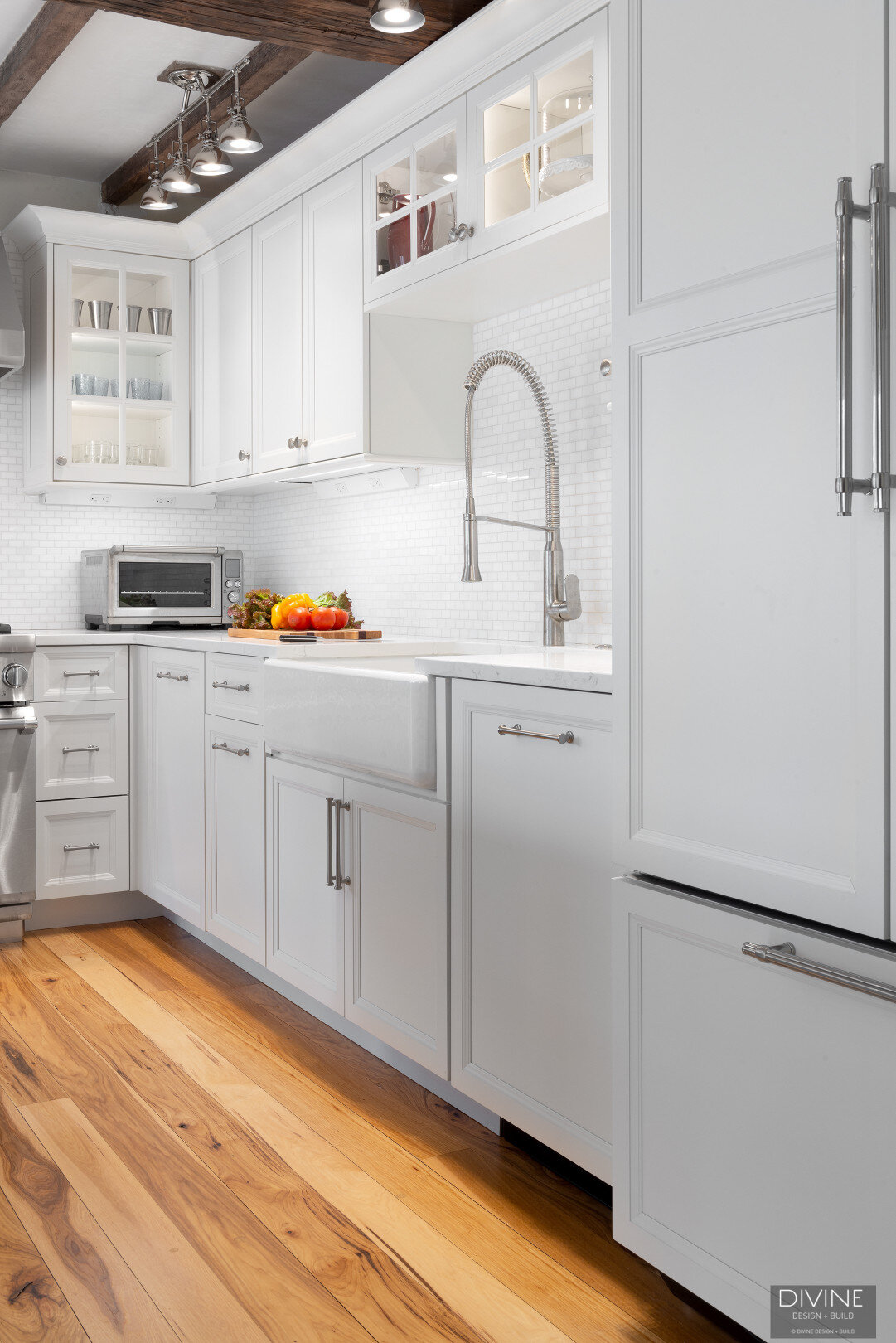 white, shaker style cabinets with brushed nickel accessories, white mosaic subway tile backsplash, cambria countertops with light marbling in grey tone and a paneled refrigerator. 