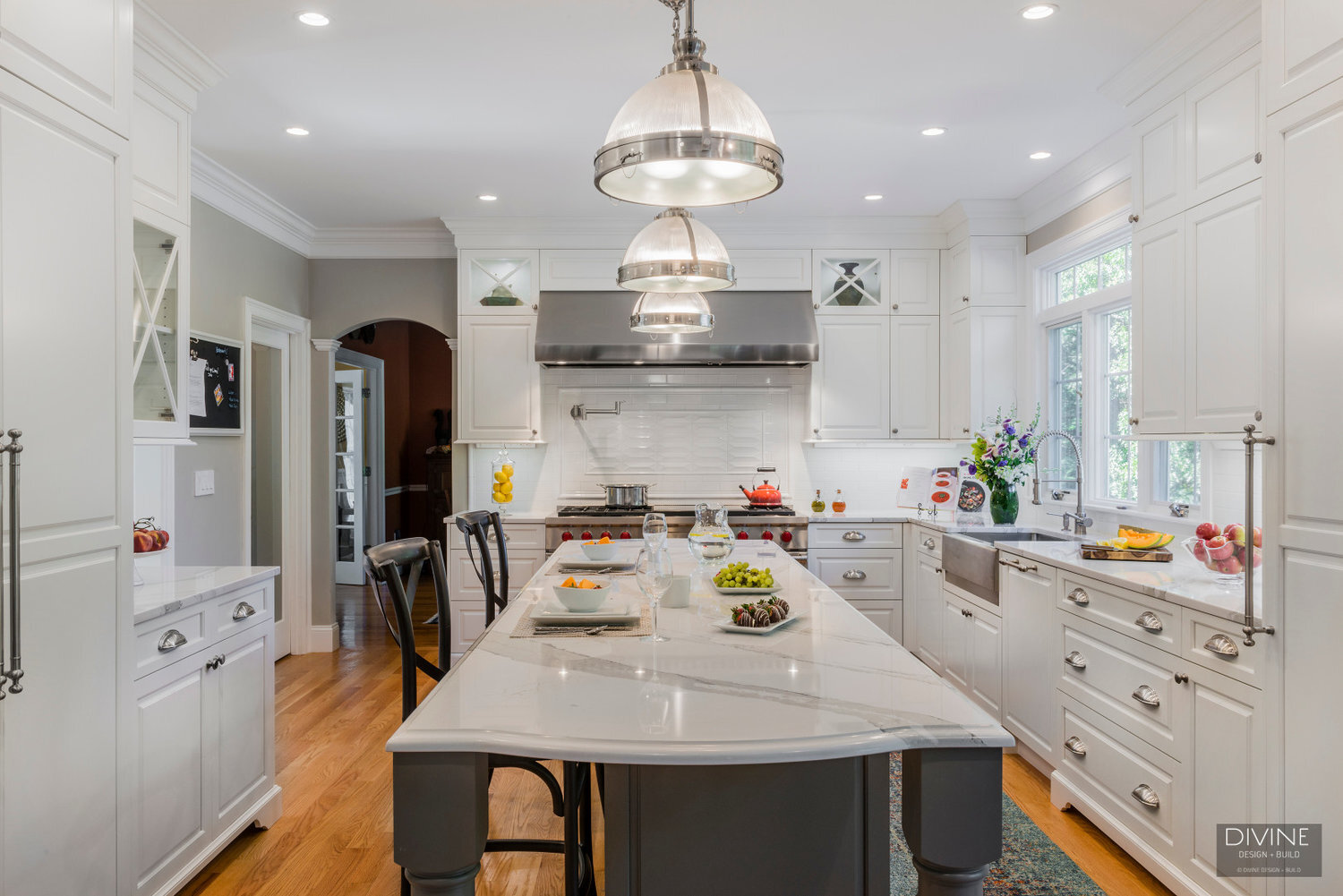  traditional shaker style kitchens with stainless steel farmhouse sink, wolf appliances and chrome pendant lights. Calacatta countertops and medium hardwood floors. Paneled refrigerator. 