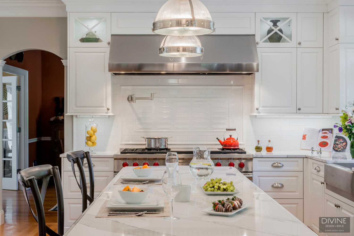 traditional shaker style kitchens with stainless steel farmhouse sink, wolf appliances and chrome pendant lights. Calacatta countertops and medium hardwood floors. Paneled refrigerator. 