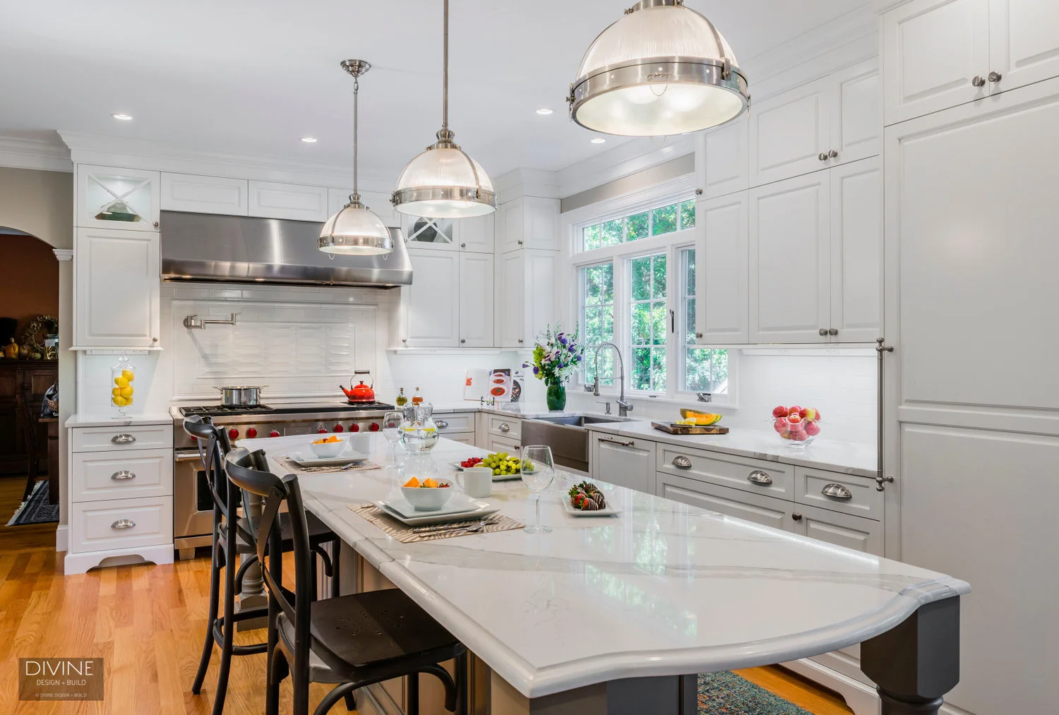  traditional shaker style kitchens with stainless steel farmhouse sink, wolf appliances and chrome pendant lights. Calacatta countertops and medium hardwood floors. Paneled refrigerator. 