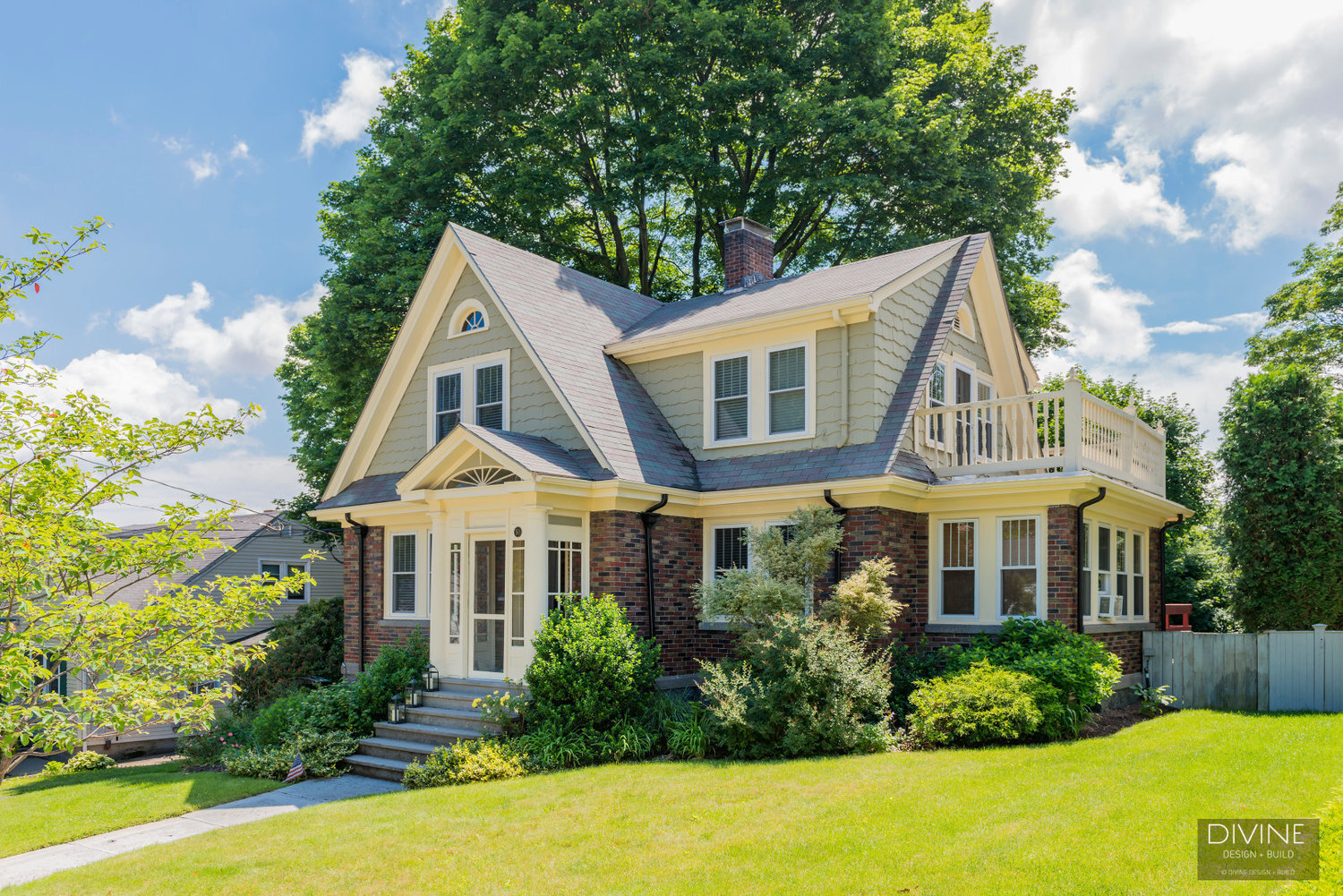  New england style home with multiple gables. Mixed siding of green shingles and brick. Off white trim and window frames. Second floor deck off the master suit.