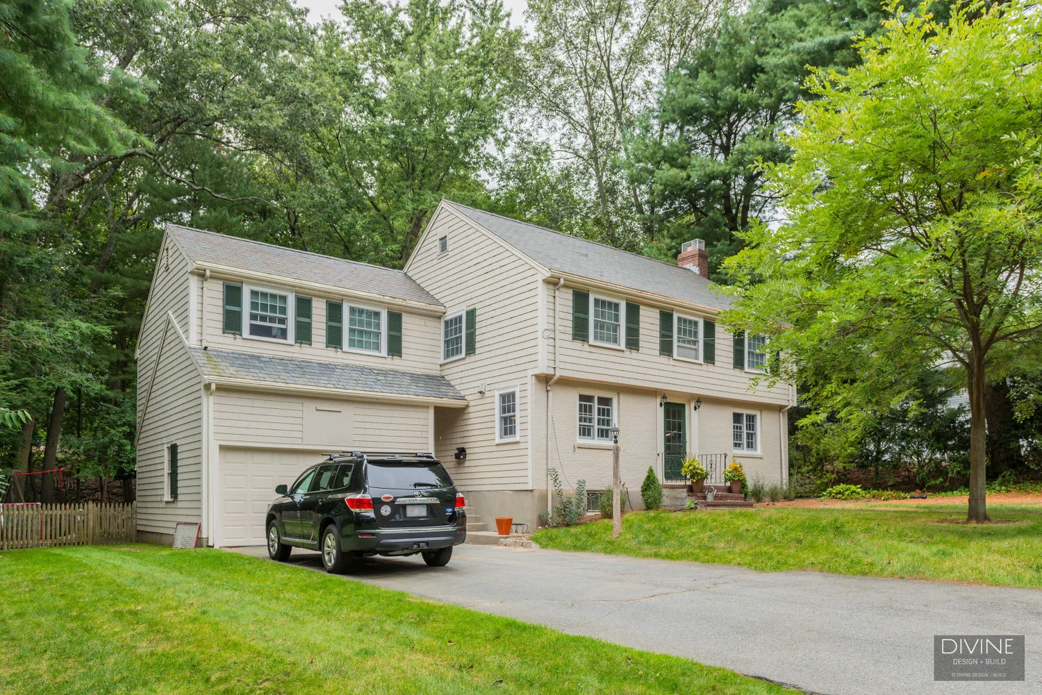 Creme painted wood siding with green shutters and colonial windows. Multi level single family home with shingled roof and two car garage. Forest green front door. 