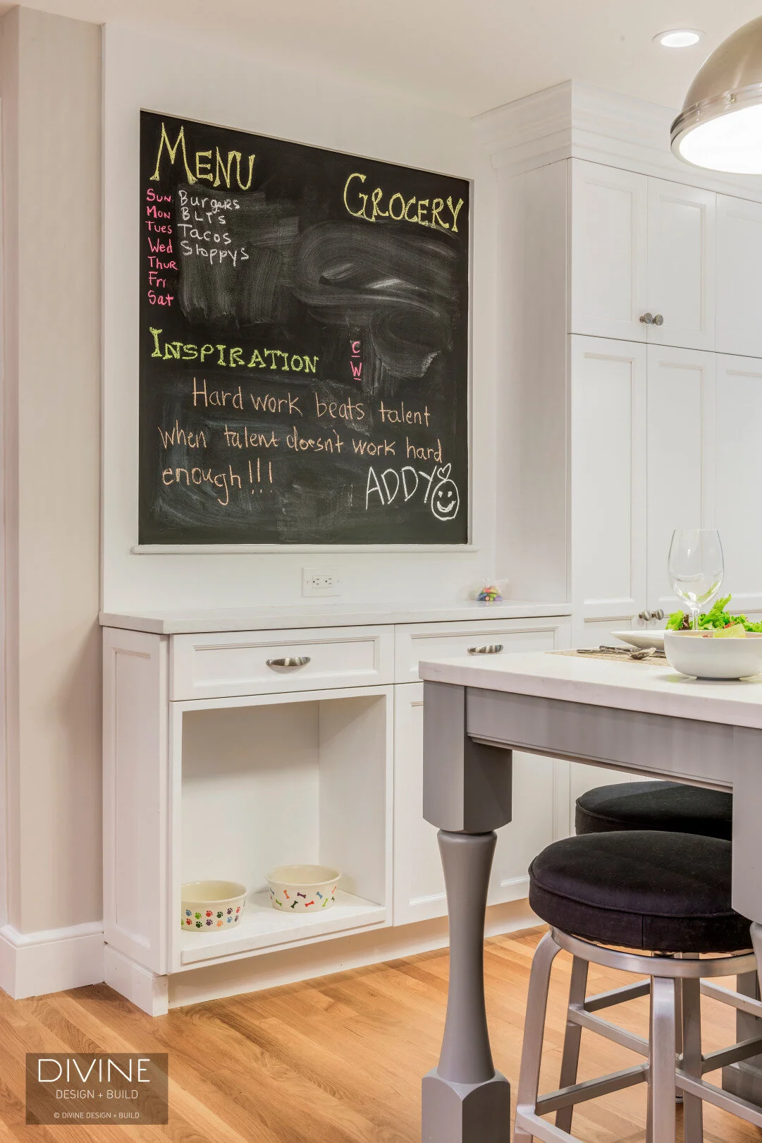  Grey and white transitional style kitchen with shaker cabinets and integrated dog feeding station. Chalkboard. Subway tile backsplash and industrial style lights and shelving