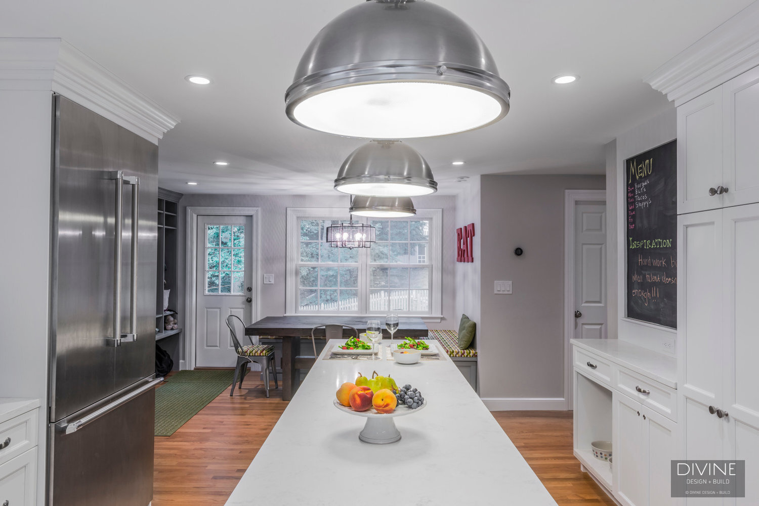  Grey and white transitional style kitchen with shaker cabinets and integrated dog feeding station. Chalkboard. Subway tile backsplash and industrial style lights and shelving