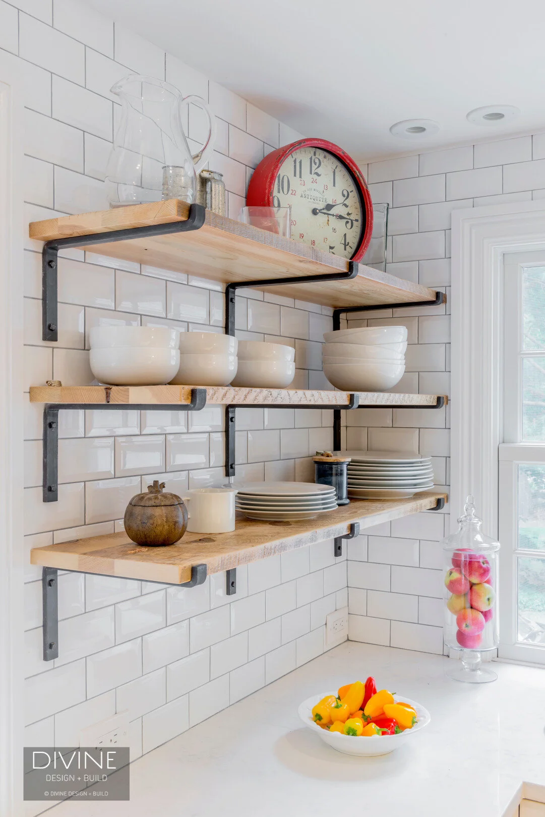 Grey and white transitional style kitchen with shaker cabinets and integrated dog feeding station. Chalkboard. Subway tile backsplash and industrial style lights and shelving