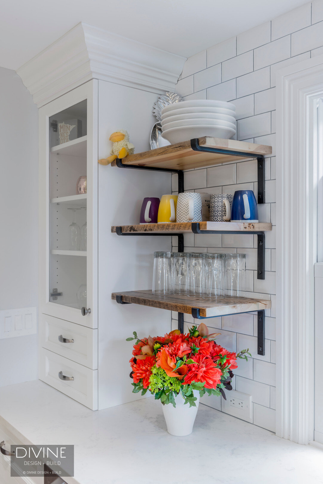 Grey and white transitional style kitchen with shaker cabinets and integrated dog feeding station. Chalkboard. Subway tile backsplash and industrial style lights and shelving