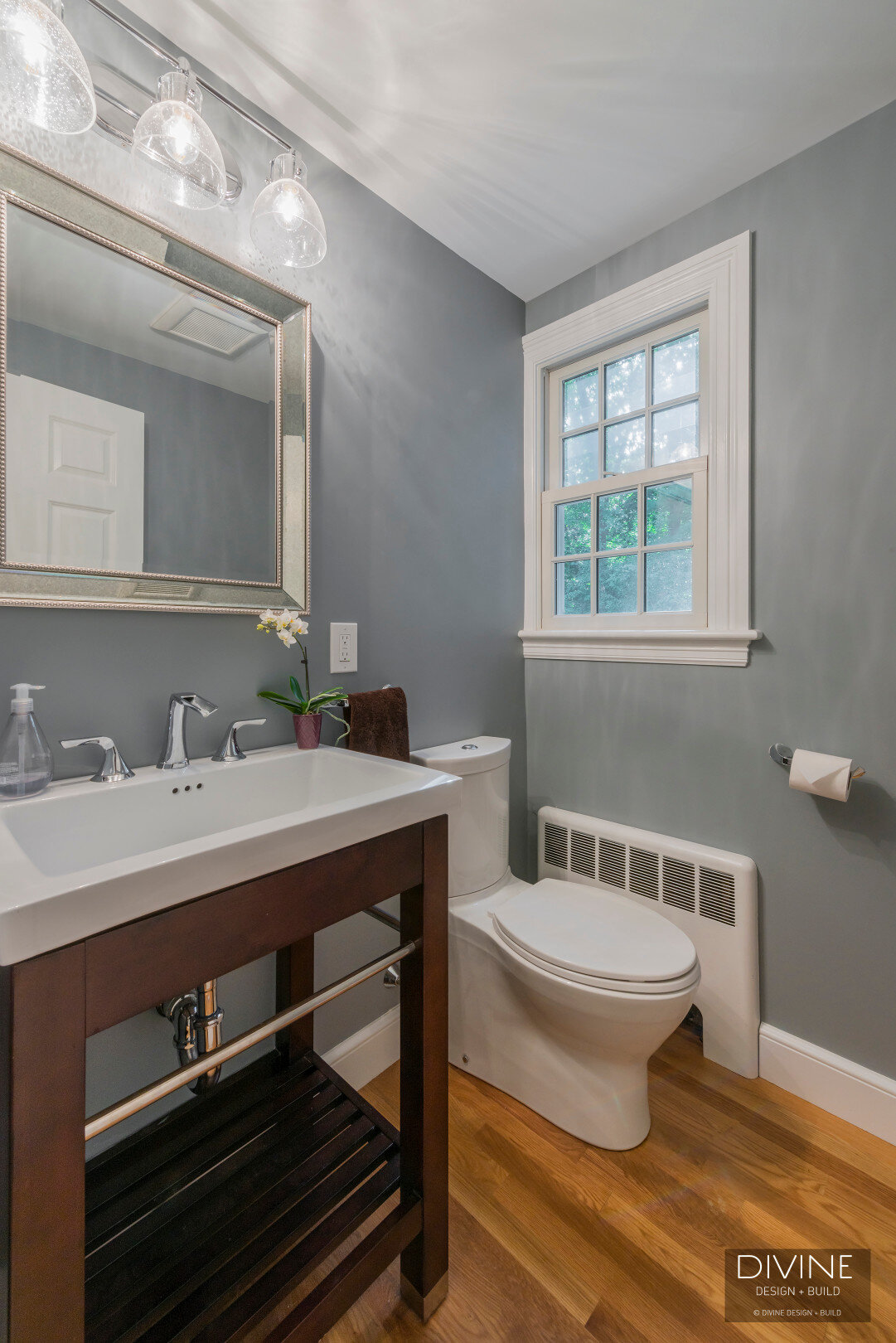  Powder room with transitional style vanity of dark wood and white porcelain sink basin. Blue wall paint. medium hardwood floors.