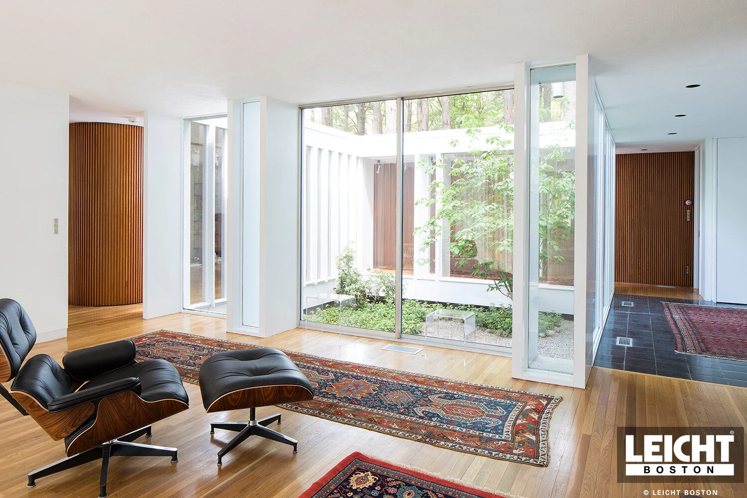  Mid century modern living room with herman miller's eames chair in black leather seat with walnut structure. hardwood floors and view of open courtyard in the middle of home.