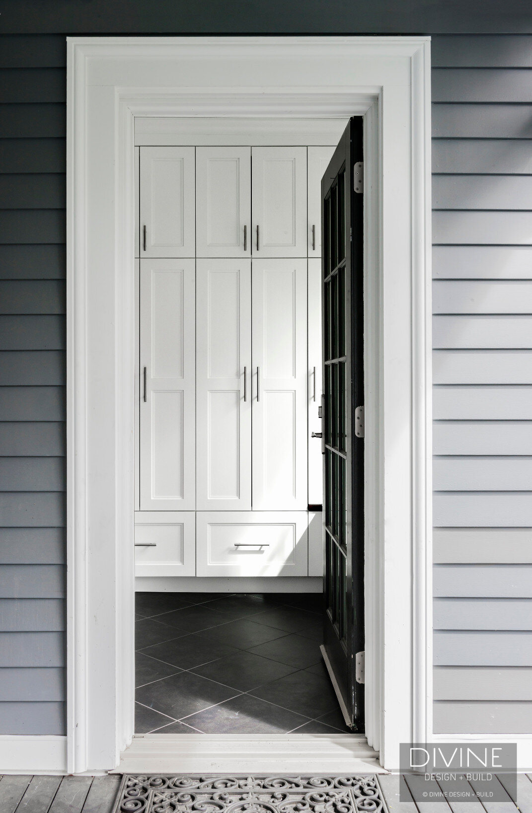 Entryway mudroom with slate tile floors, bench seating and tall white shaker cabinets