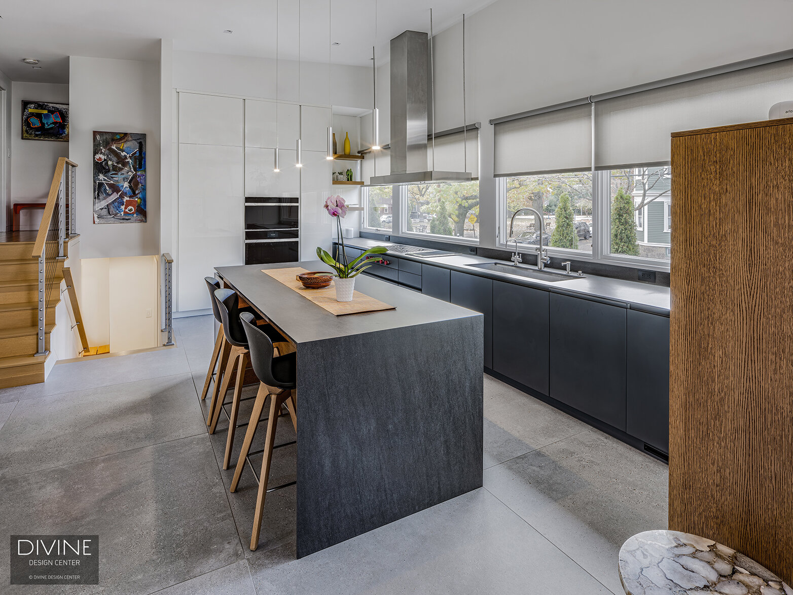  black Leicht kitchen with complementing dark hardwood veneer and white, high gloss accent cabinet fronts. Waterfall kitchen island top with stainless steel appliances and hood. Concrete floors, a paneled refrigerator, handleless cabinets, and large 
