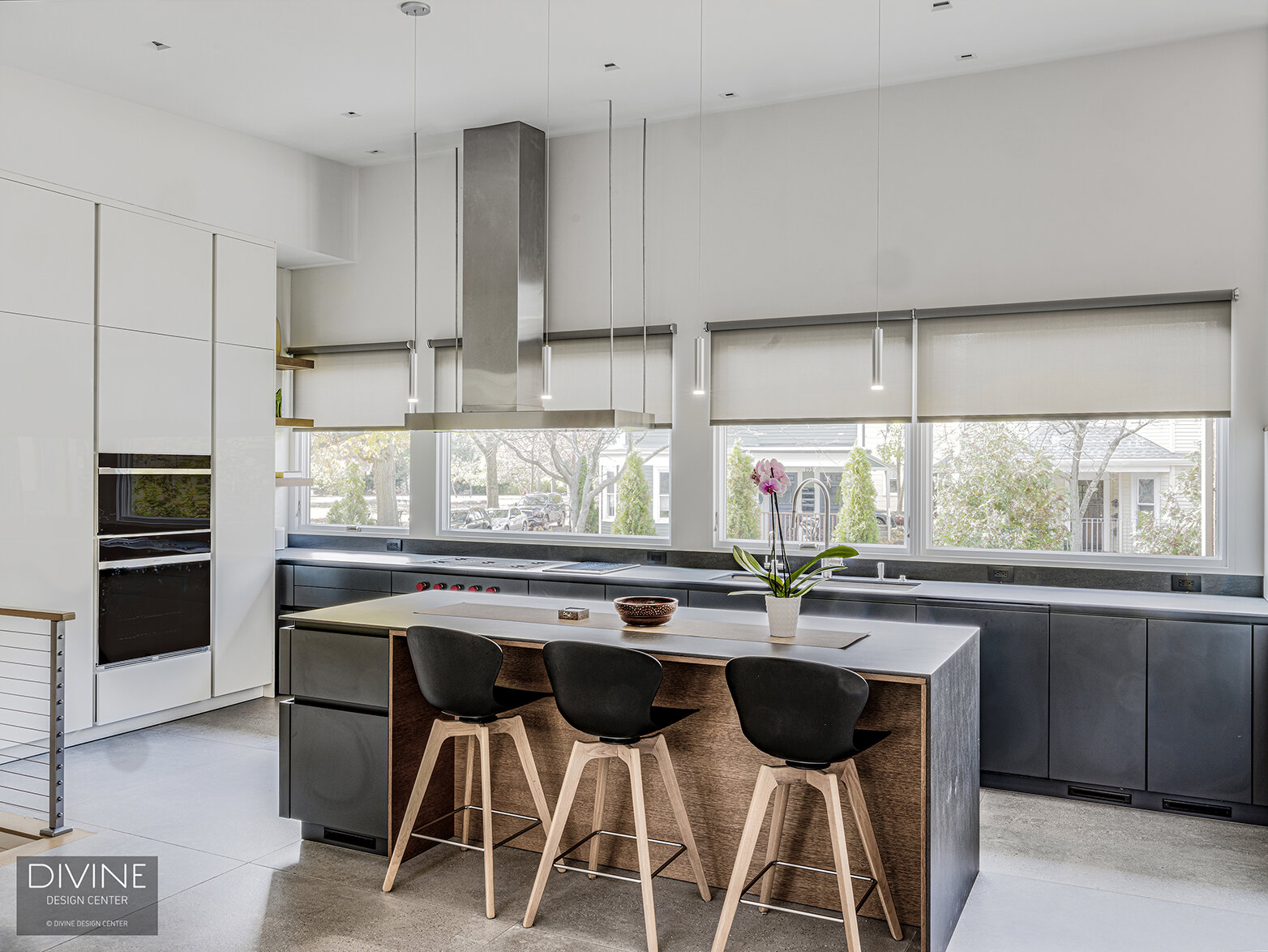  black Leicht kitchen with complementing dark hardwood veneer and white, high gloss accent cabinet fronts. Waterfall kitchen island top with stainless steel appliances and hood. Concrete floors, a paneled refrigerator, handleless cabinets, and large 