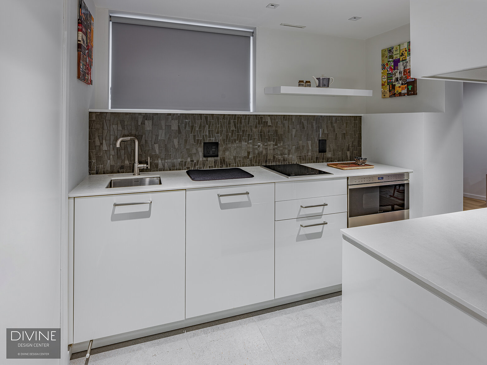  The wet bar with a gray mosaic-like backsplash is surrounded by high gloss, white lacquered cabinets with stainless steel handles and knobs. A wine refrigerator and floating shelves round out this carved out space.  