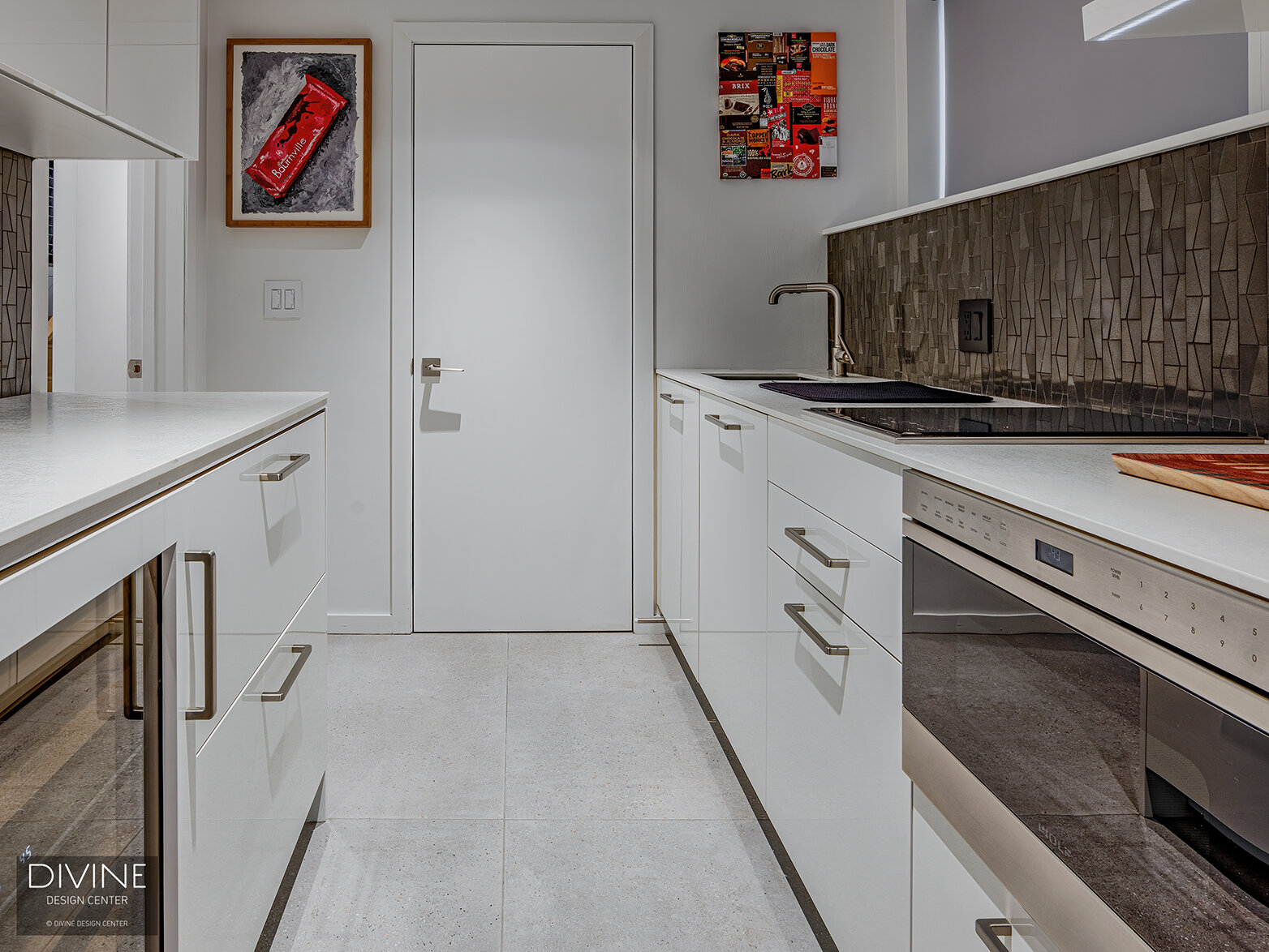  The wet bar with a gray mosaic-like backsplash is surrounded by high gloss, white lacquered cabinets with stainless steel handles and knobs. A wine refrigerator and floating shelves round out this carved out space. Red accent art is displayed on eac