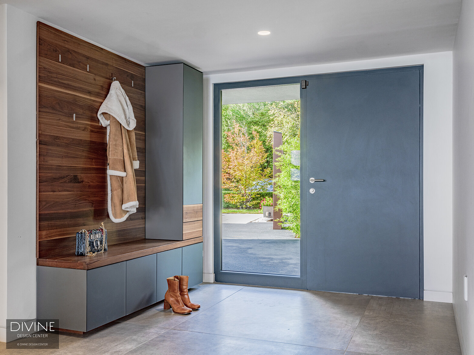  modern entryway with grey, Leicht cabinetry, and a walnut bench.  A large glass window flanks a wide, tall modern, European door that is flush to its surround. White walls and small recessed overhead lights accompany the space.  