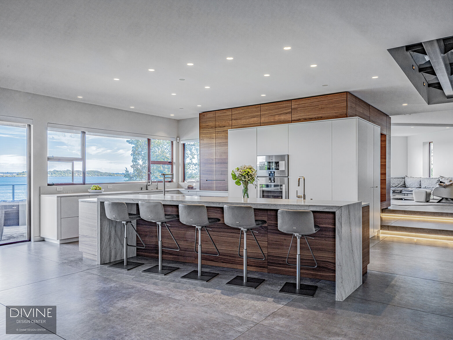  Modern, Leicht kitchen with an extra large, waterfall kitchen island sitting five. A calacatta marble island top pairs with a walnut toe kick and walnut accents throughout the space. High gloss, white paneled kitchen cabinets hide the refrigerator a