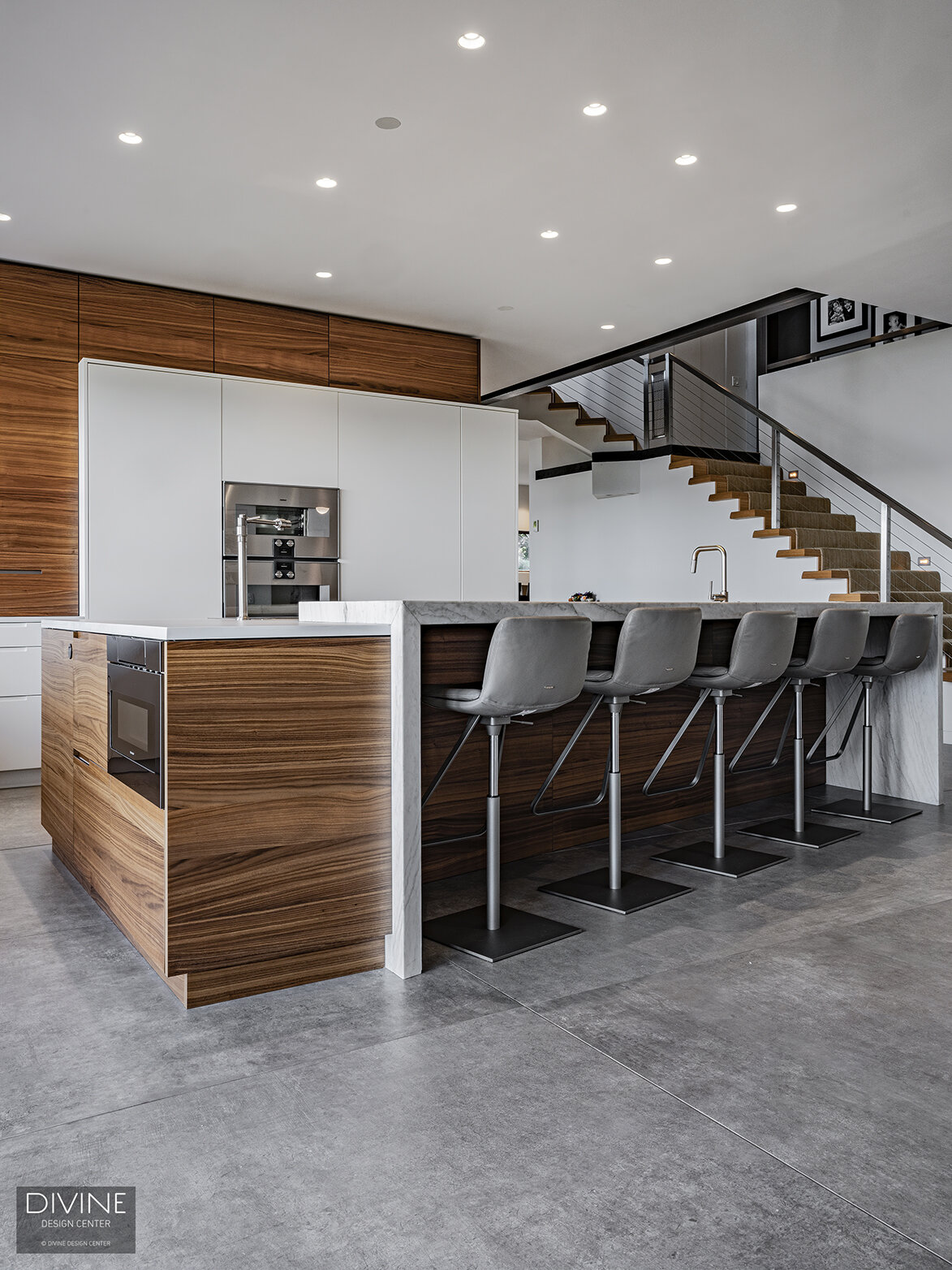  Modern, Leicht kitchen with an extra-large, waterfall kitchen island sitting five. A Calcutta marble island top pairs with a walnut toe kick and walnut accents throughout the space. High gloss, white paneled kitchen cabinets hide the refrigerator an