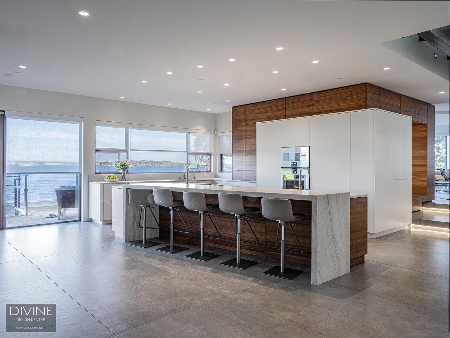  Modern, Leicht kitchen with an extra-large, waterfall kitchen island sitting five. A Calcutta marble island top pairs with a walnut toe kick and walnut accents throughout the space. High gloss, white paneled kitchen cabinets hide the refrigerator an