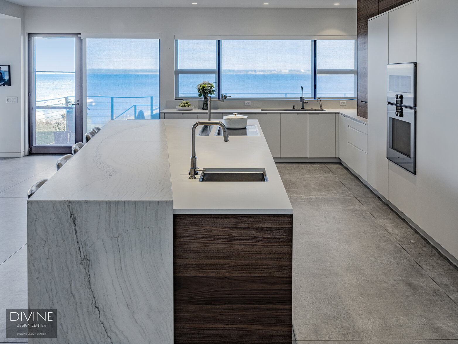  Modern, Leicht kitchen with an extra-large, waterfall kitchen island sitting five. A Calcutta marble island top pairs with a walnut toe kick and walnut accents throughout the space. High gloss, white paneled kitchen cabinets hide the refrigerator an