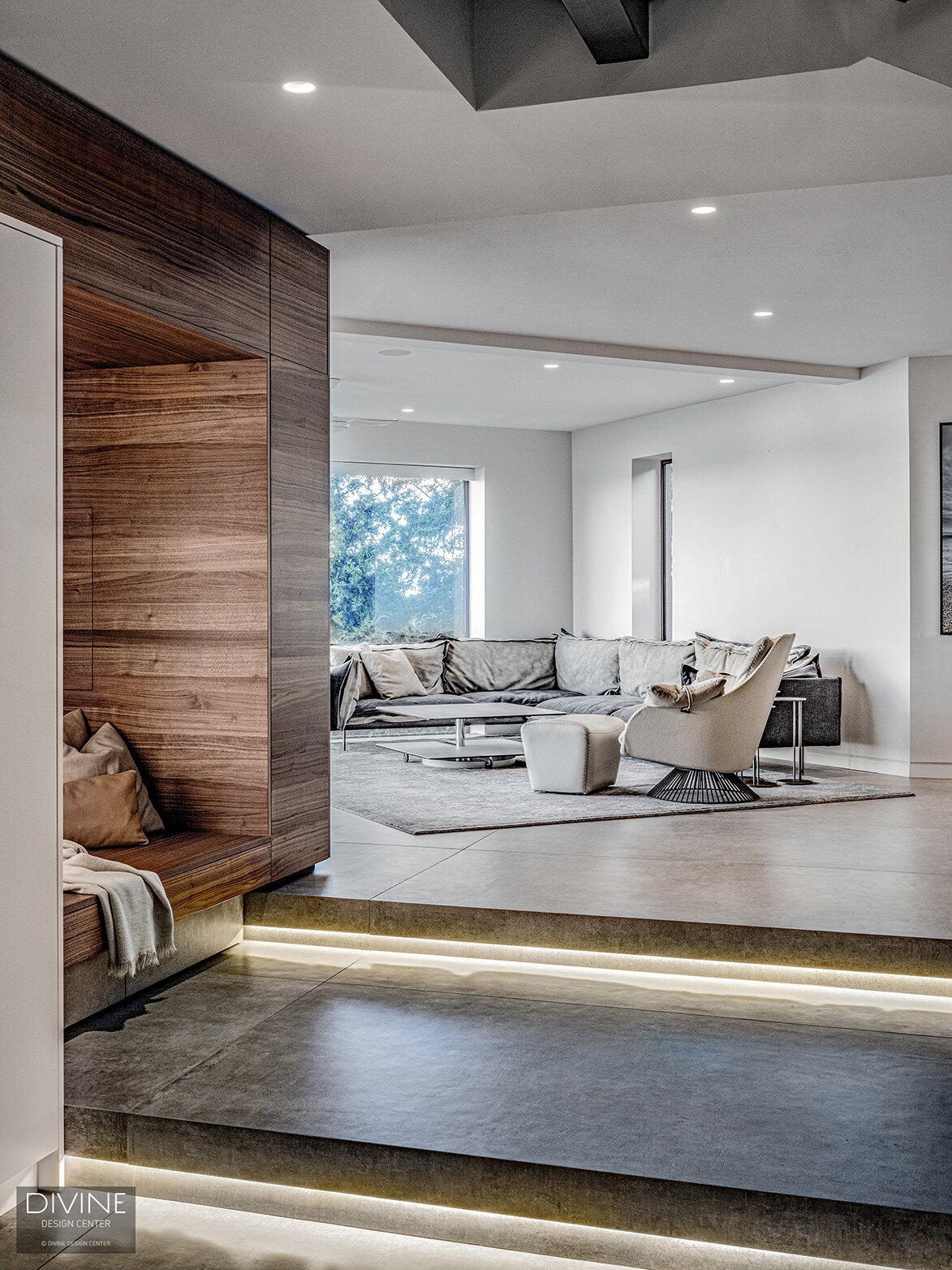  A niche seating area in walnut in the forefront in the step down of a concrete step with architectural lighting below - in the background is a large living area in cool, grey tones with Leolux and Rolf Benz furniture of a similar modern style. A lar