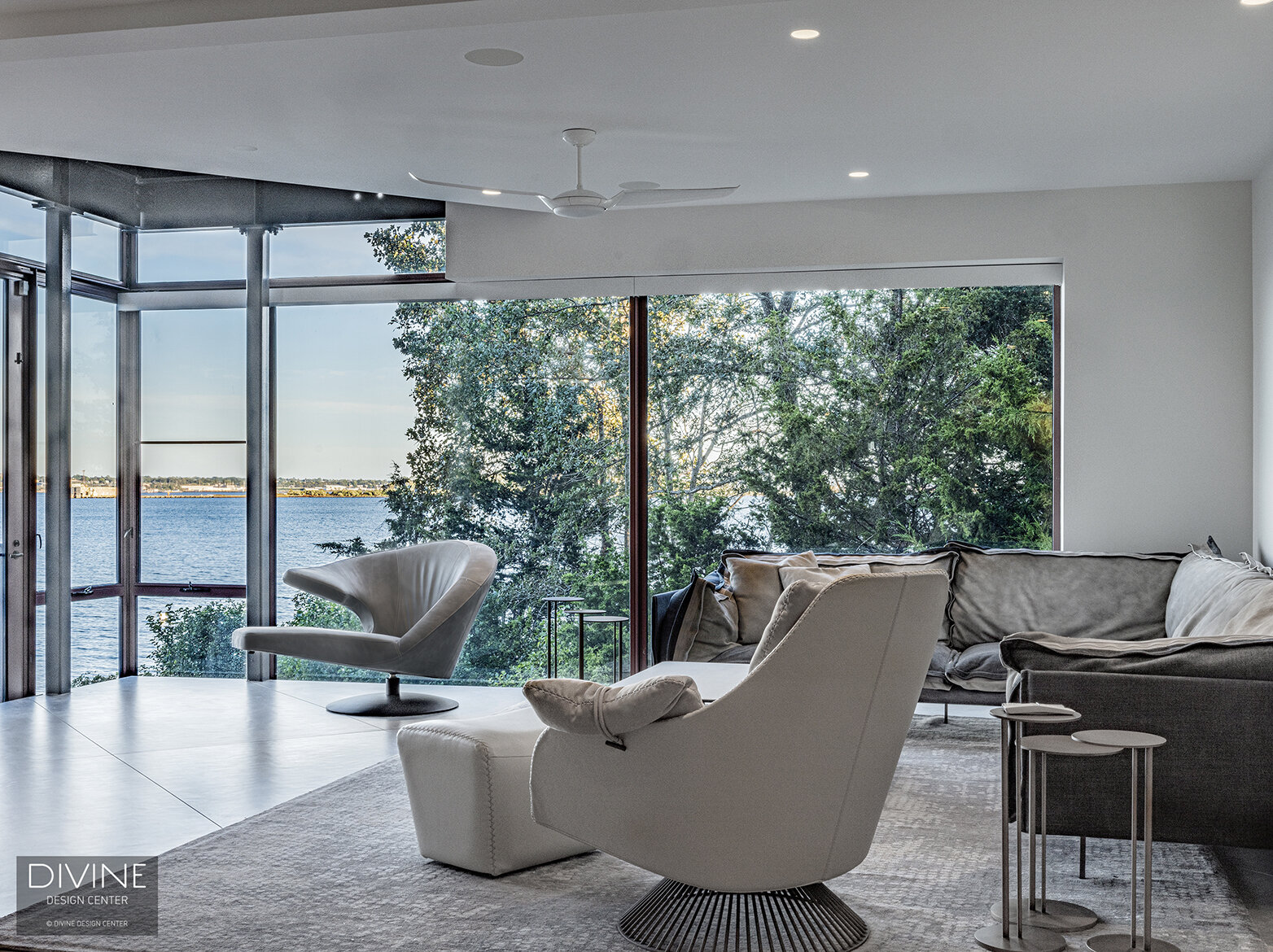  A modern living room with sweeping ocean views displayed through large, glass windows. Arketipo Firenze sectional sofa and occasional chair pair with the iconic parabolica armchair by leolux. clustered, nesting side tables by Arketipo are highlighte