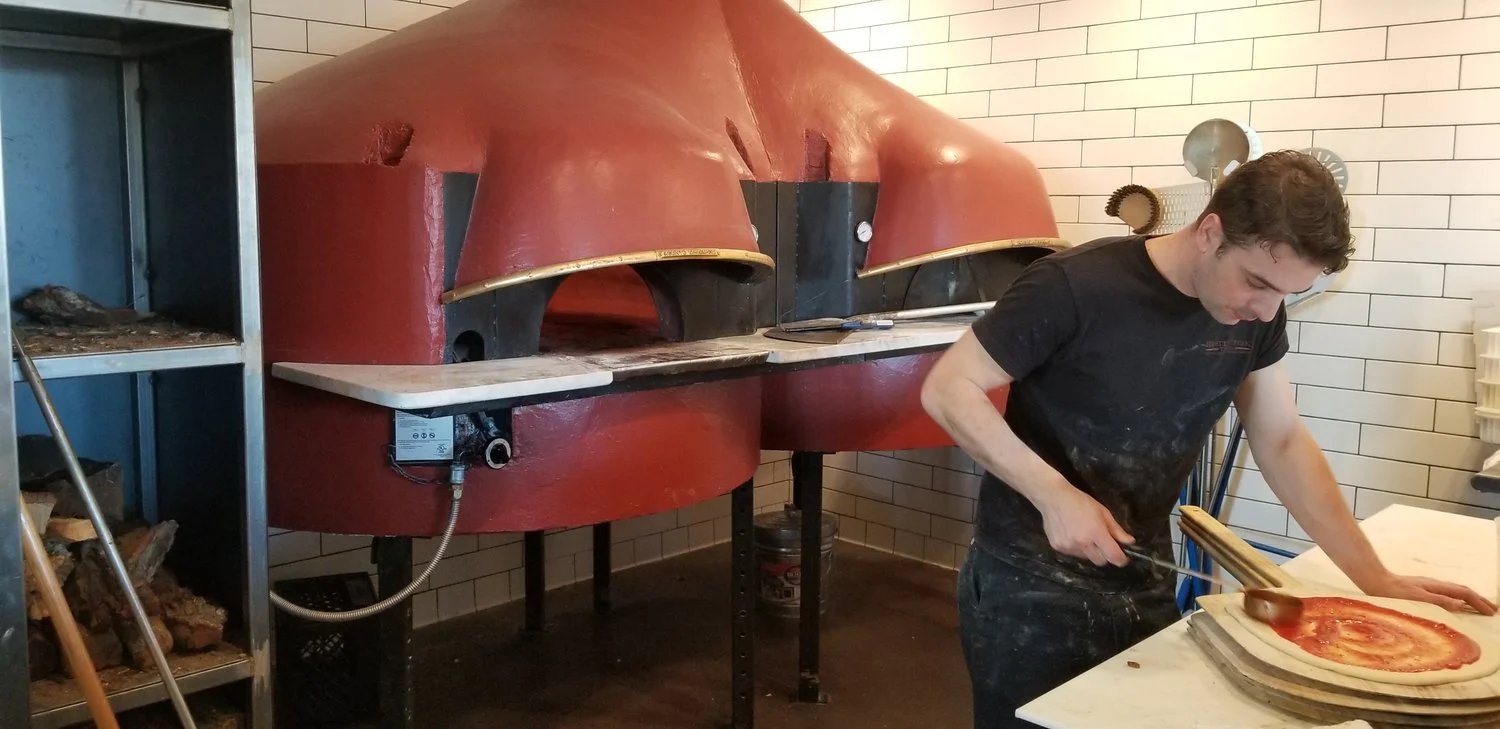 Pizza chef at work… note the stacks of wood for stocking the oven.