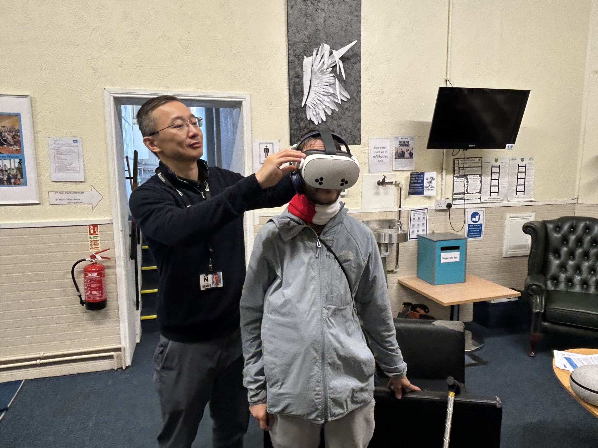 A man helps a person put on a VR headset in a room