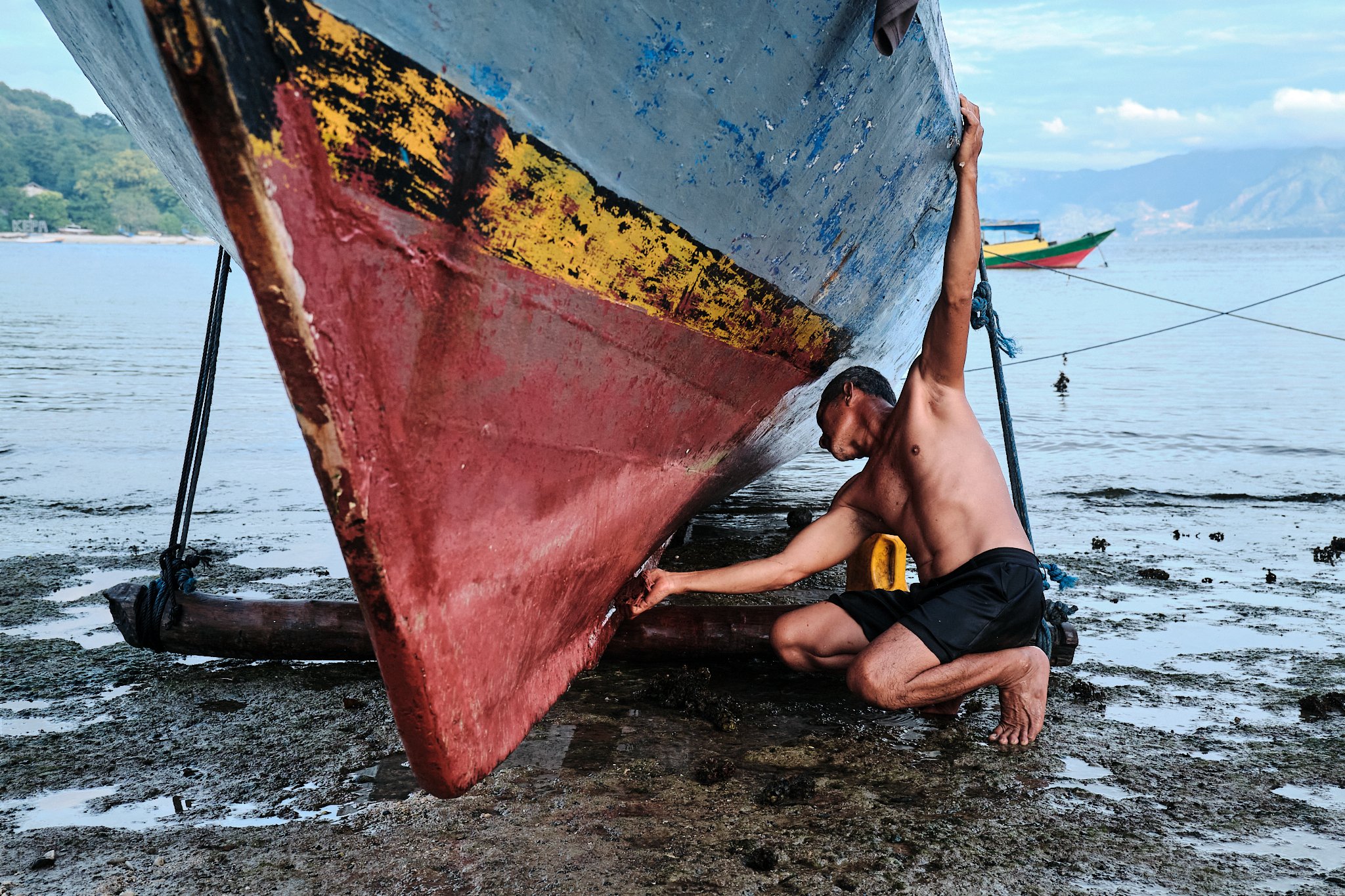 A local fisherman cleaning his boat on the shore of Alor-Kecil, Indonesia taken by travel photographer Lee Starnes