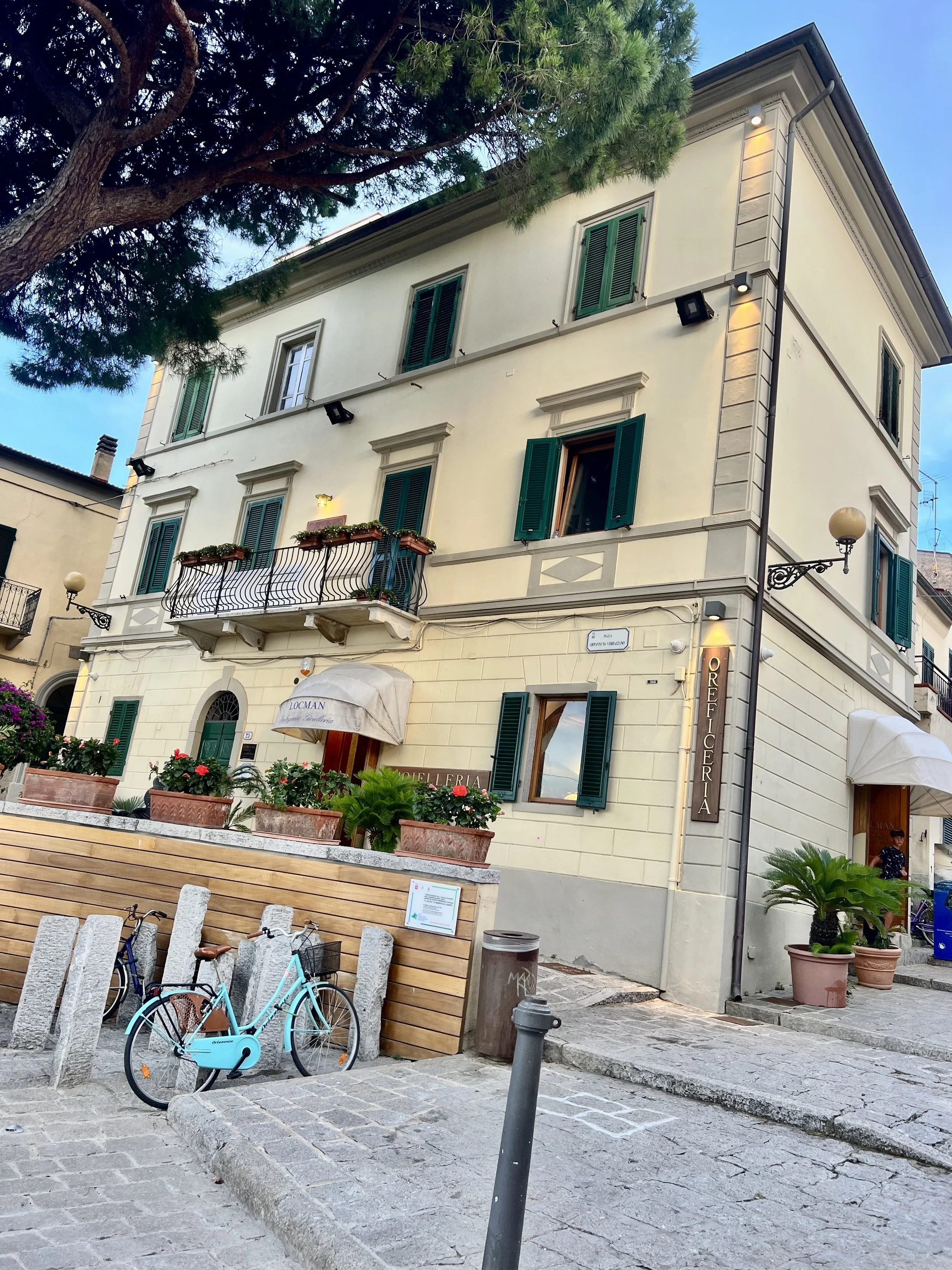 Häuserfassade mit offenem Fenster, Balkon mit Blumen, Fahrrad vor Café 'Locman', Straßenszene in Italien.