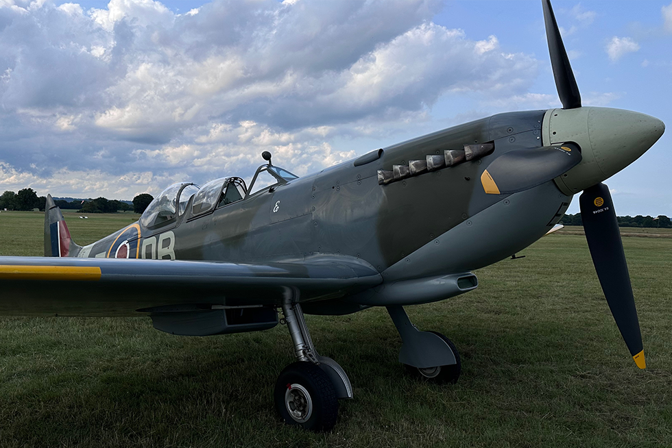 A vintage military aircraft parked on a grassy airfield under cloudy skies.