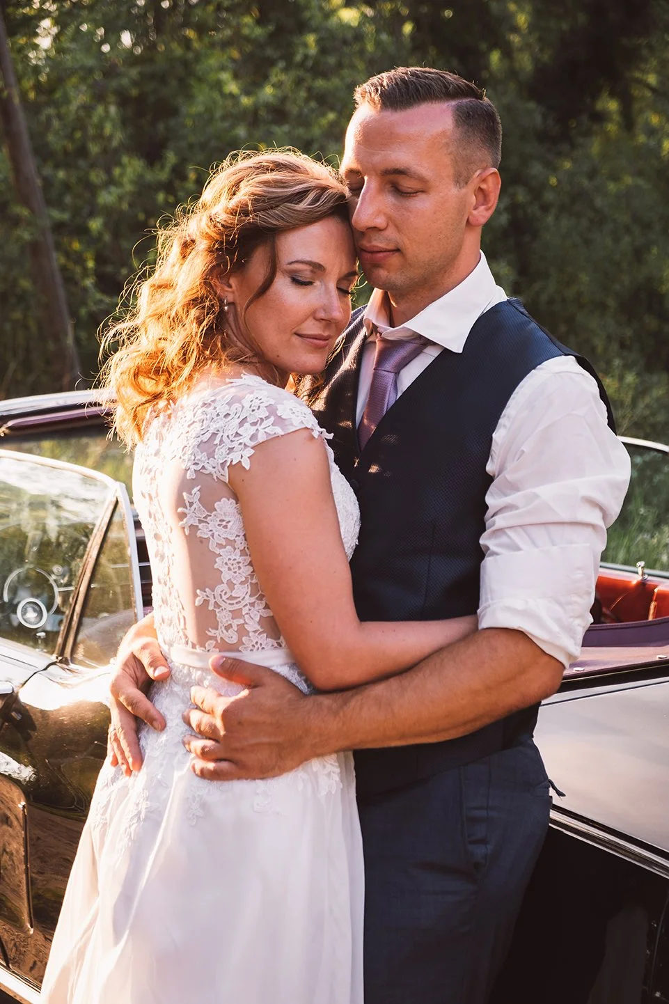 Hochzeitspaar stehend an Oldtimer schmusend