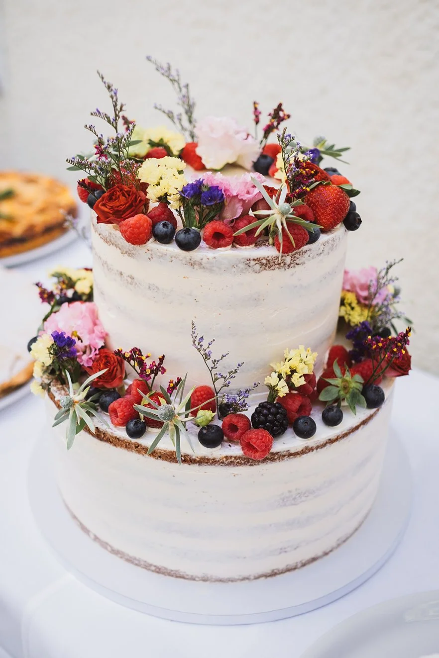 Zweistöckige Hochzeitstorte mit frischen Himbeeren Brombeeren Wildblumen