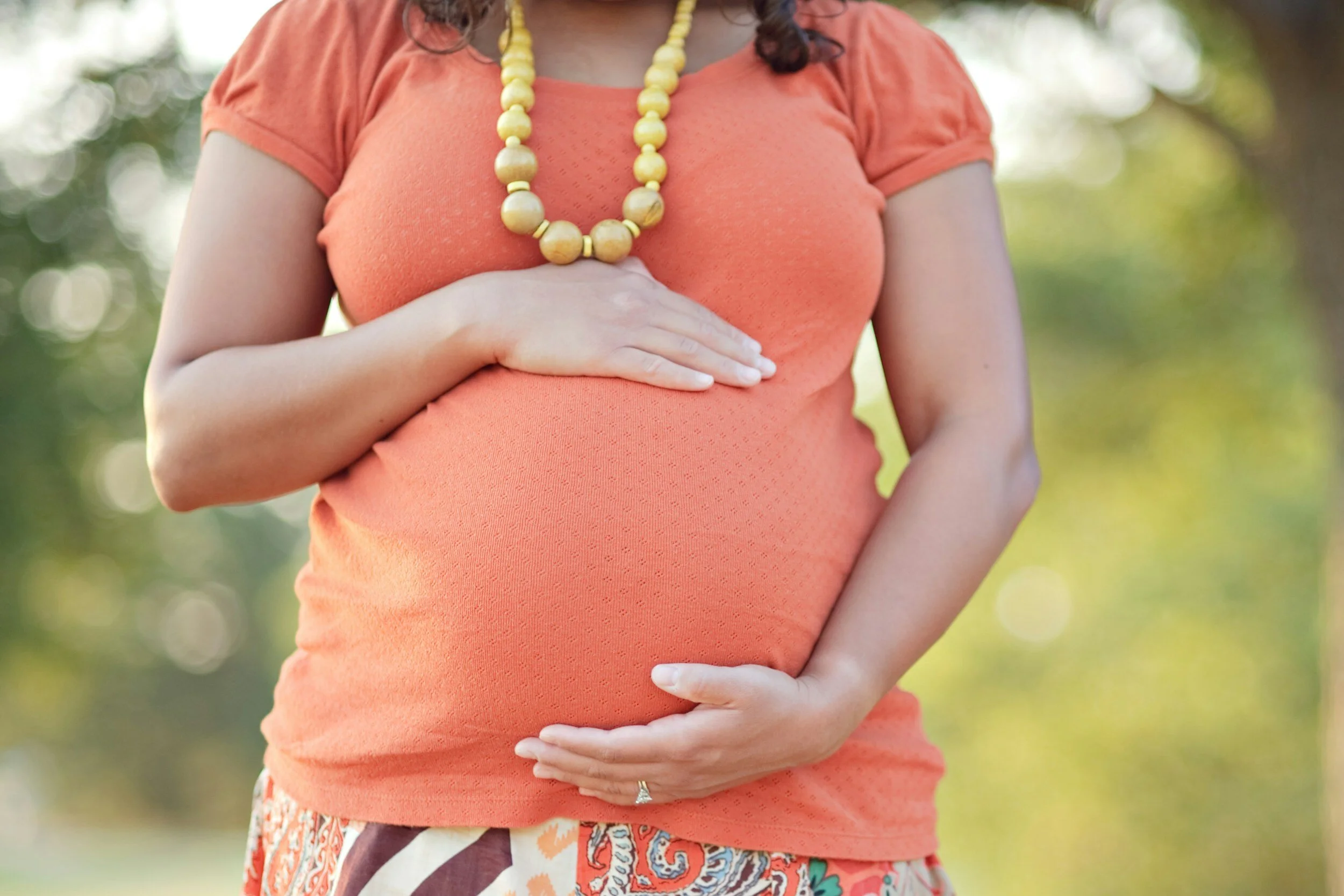 a pregnant mother holding her abdomen with one hand on top and one hand on bottom wearing an orange shirt
