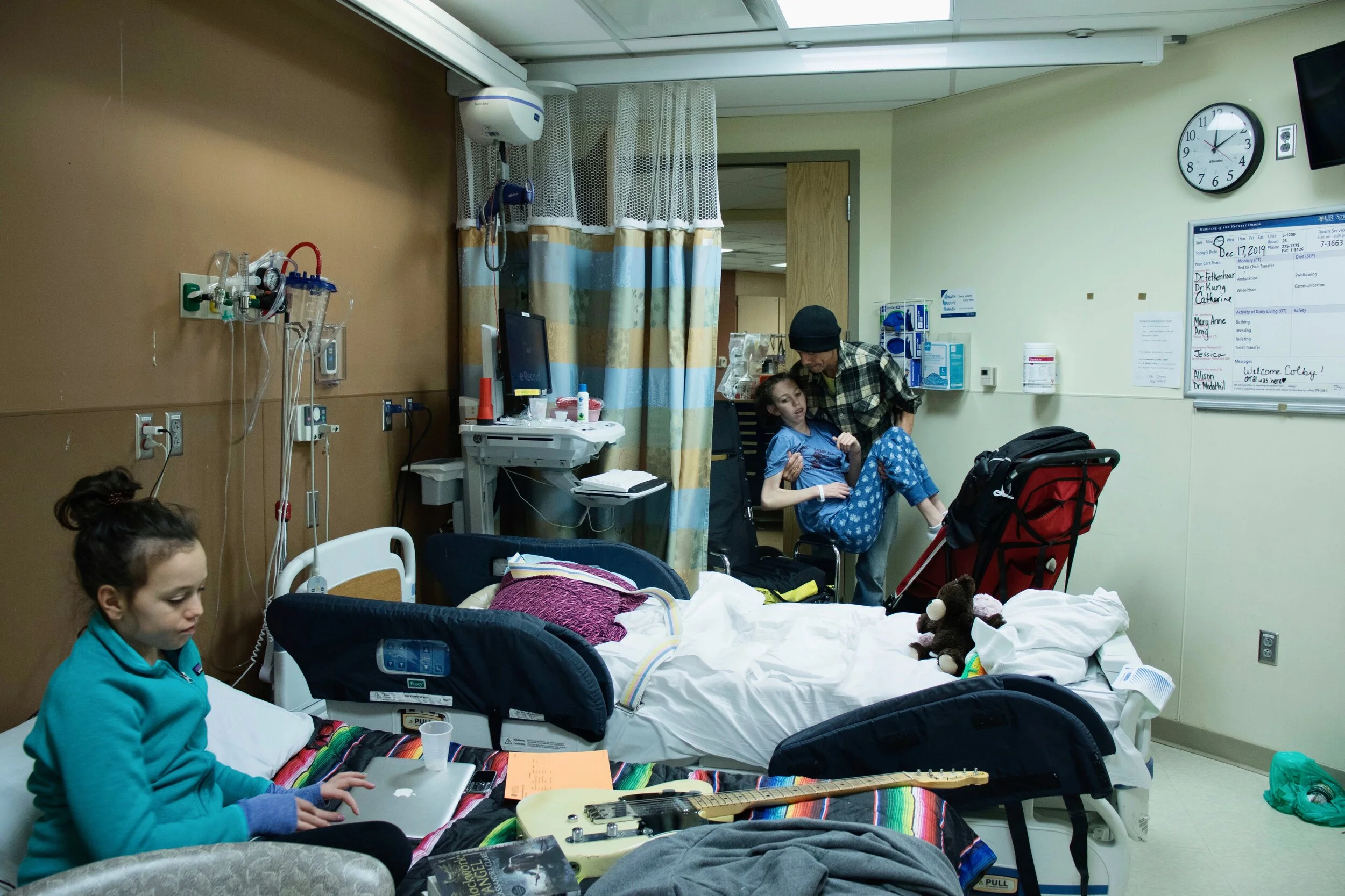 Craig Street (65) carries his daughter, Colby Street (14) from her stroller to her bed, while 11-year-old sister, Coral Street (11), occupies her time. 