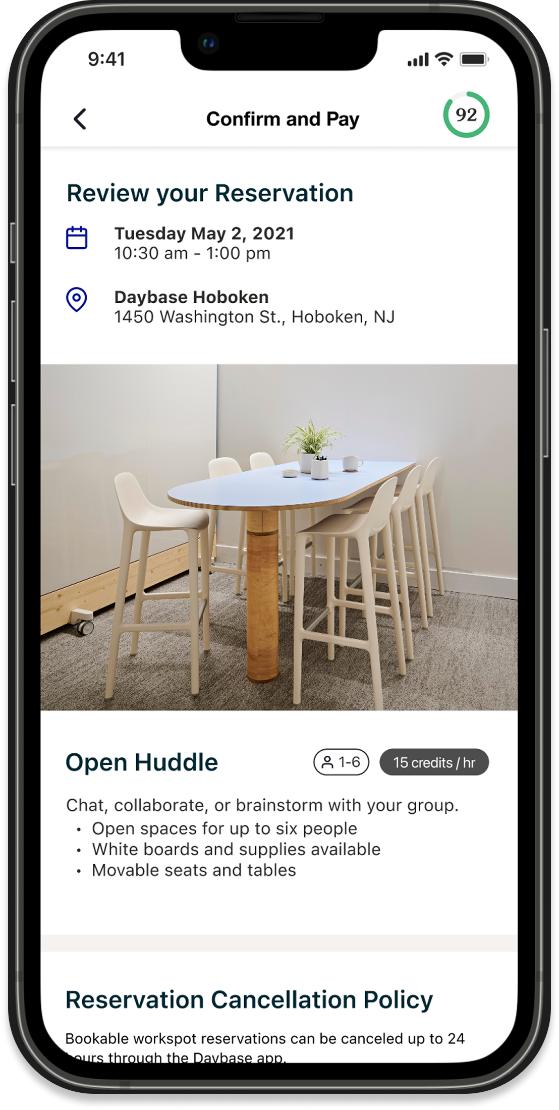 Screenshot of a mobile app showing a reservation confirmation for a meeting space, with date, time, location, and details of the space including a table with chairs and decorative plants.