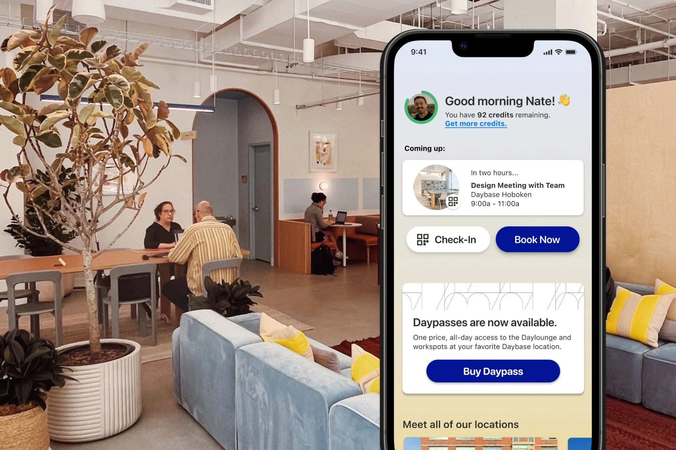 A smartphone displaying a Daybase app screen with booking information in a modern coworking space interior with people working at tables, plants, and comfortable seating.