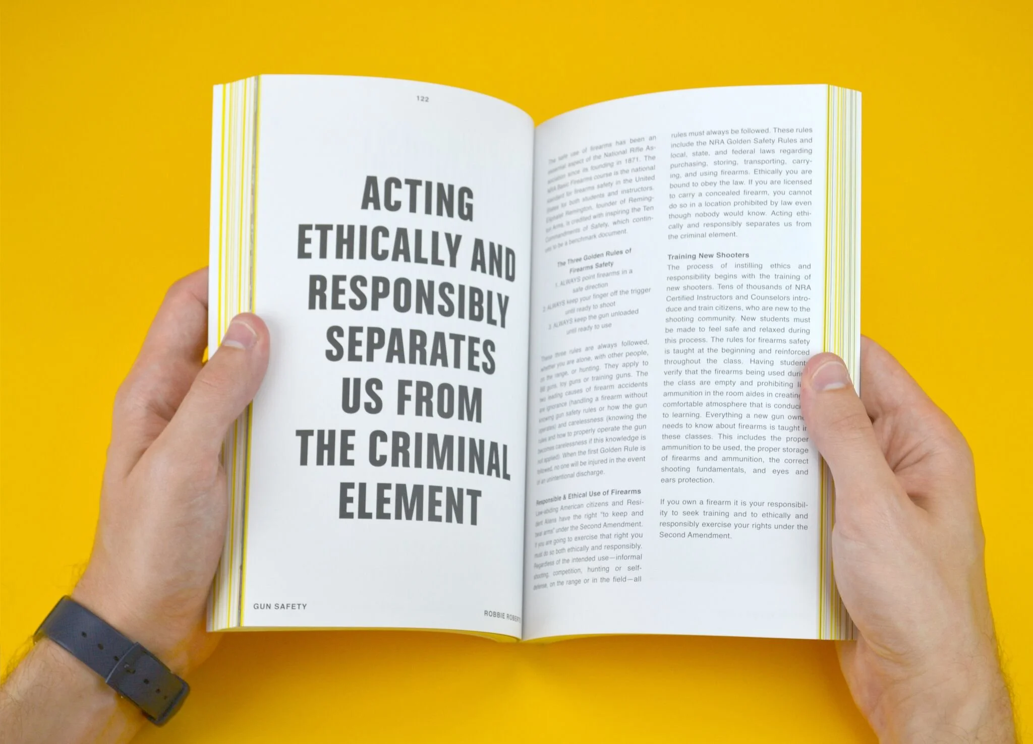 Open book with headline 'Acting Ethically and Responsibly Separates Us From the Criminal Element' on the left page and text about firearm safety and responsible gun ownership on the right page, held by person wearing a black watch, against a yellow background.