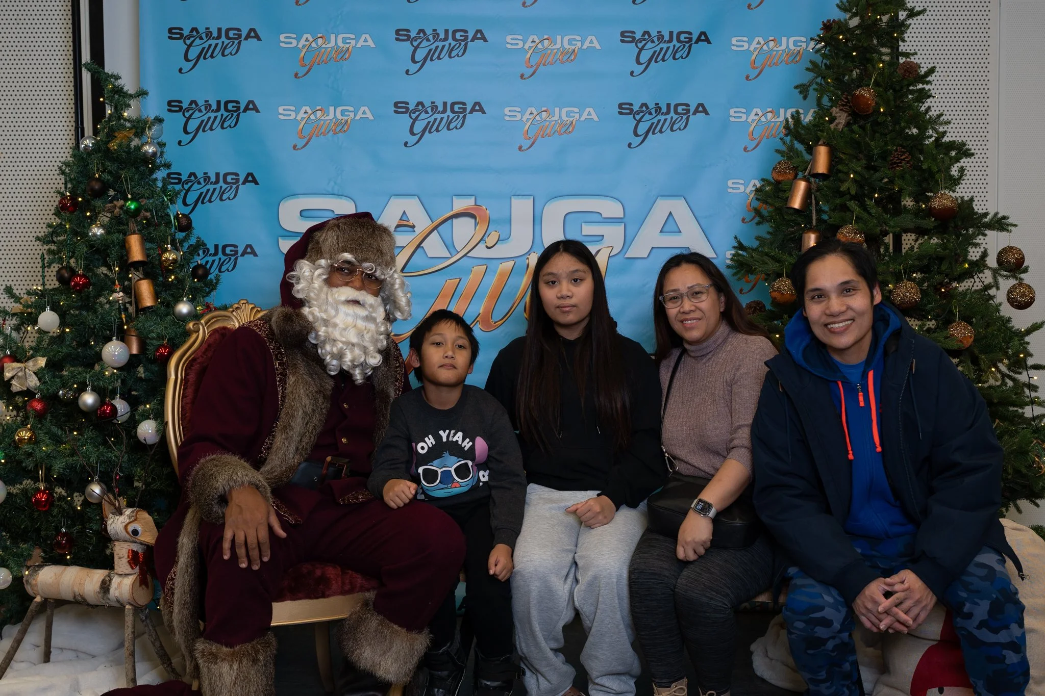 A family of four sitting with Santa in front of Christmas tree trees at the 2025 Sauga Gives Christmas event