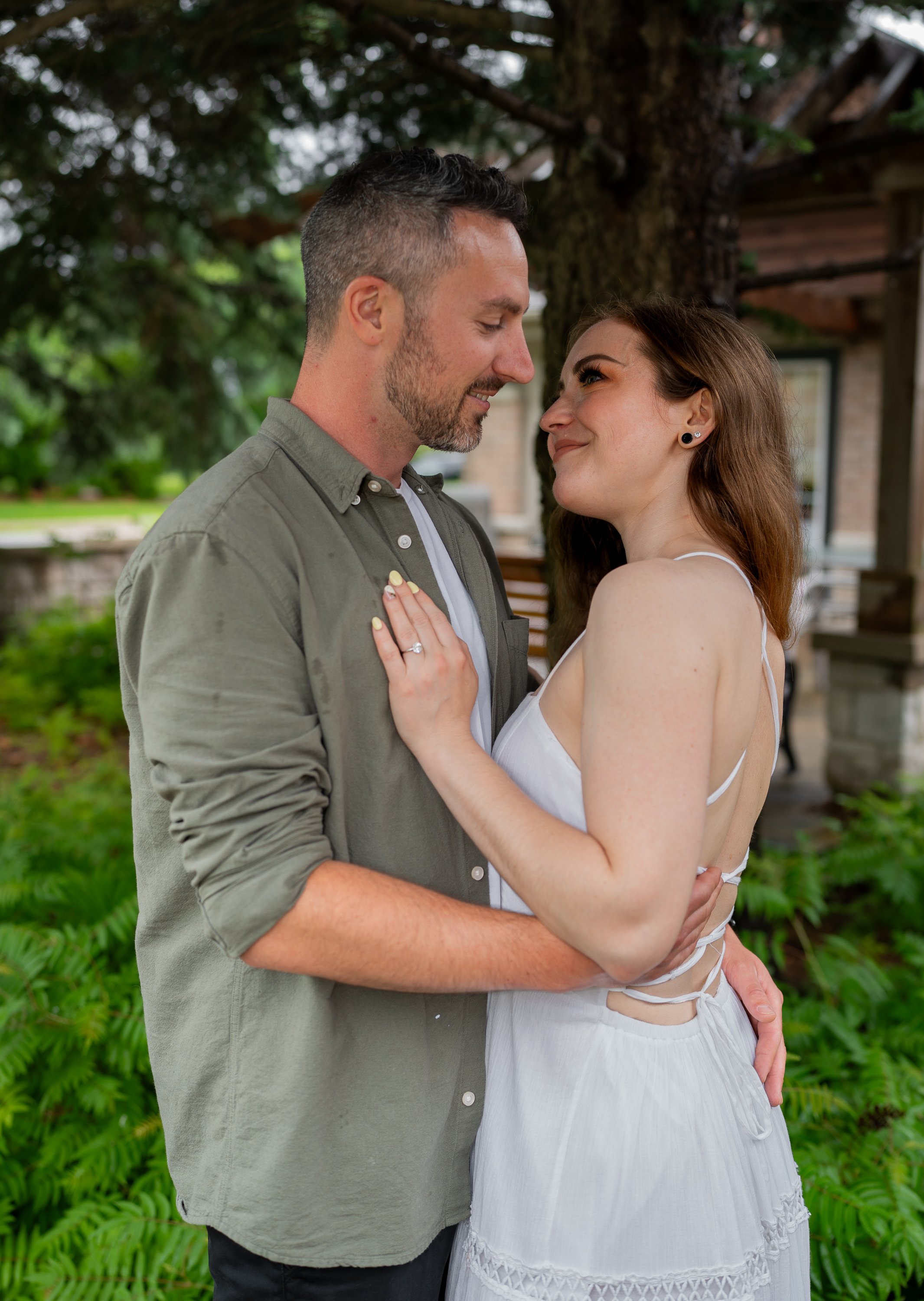 A couple standing under a tree taking  engagement photos.