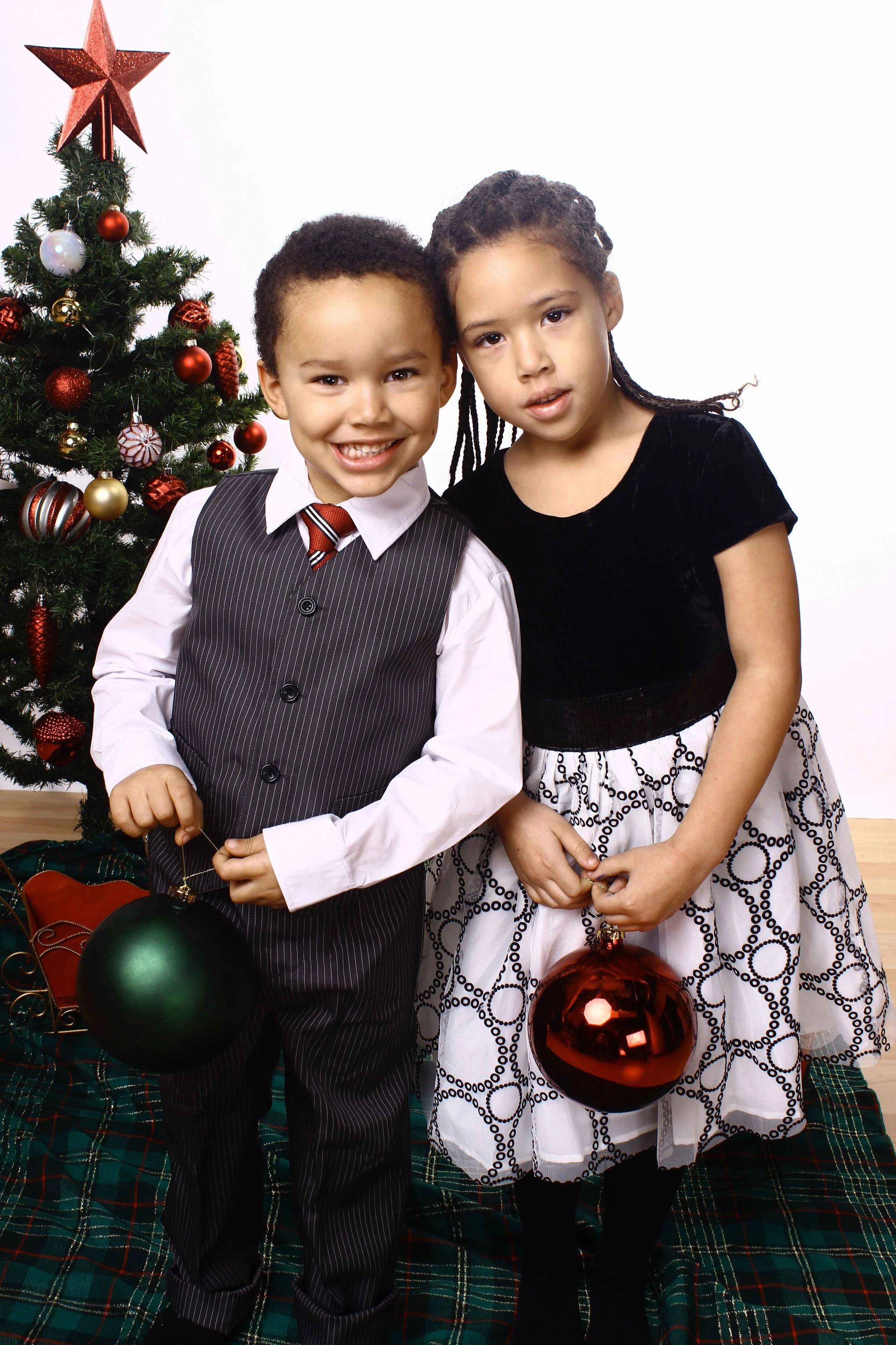 A young boy and girl standing with large Christmas ornaments in their hands for a mini holiday photo shoot